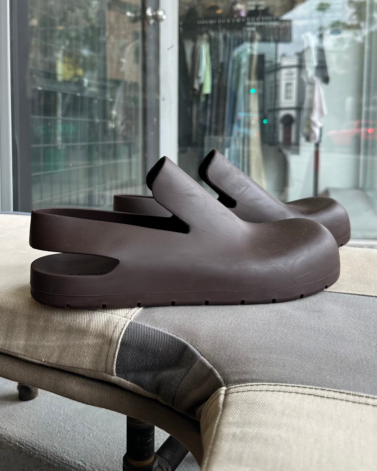 Brown Bottega Veneta clog shoe on a light gray cushion against a textured gray wall