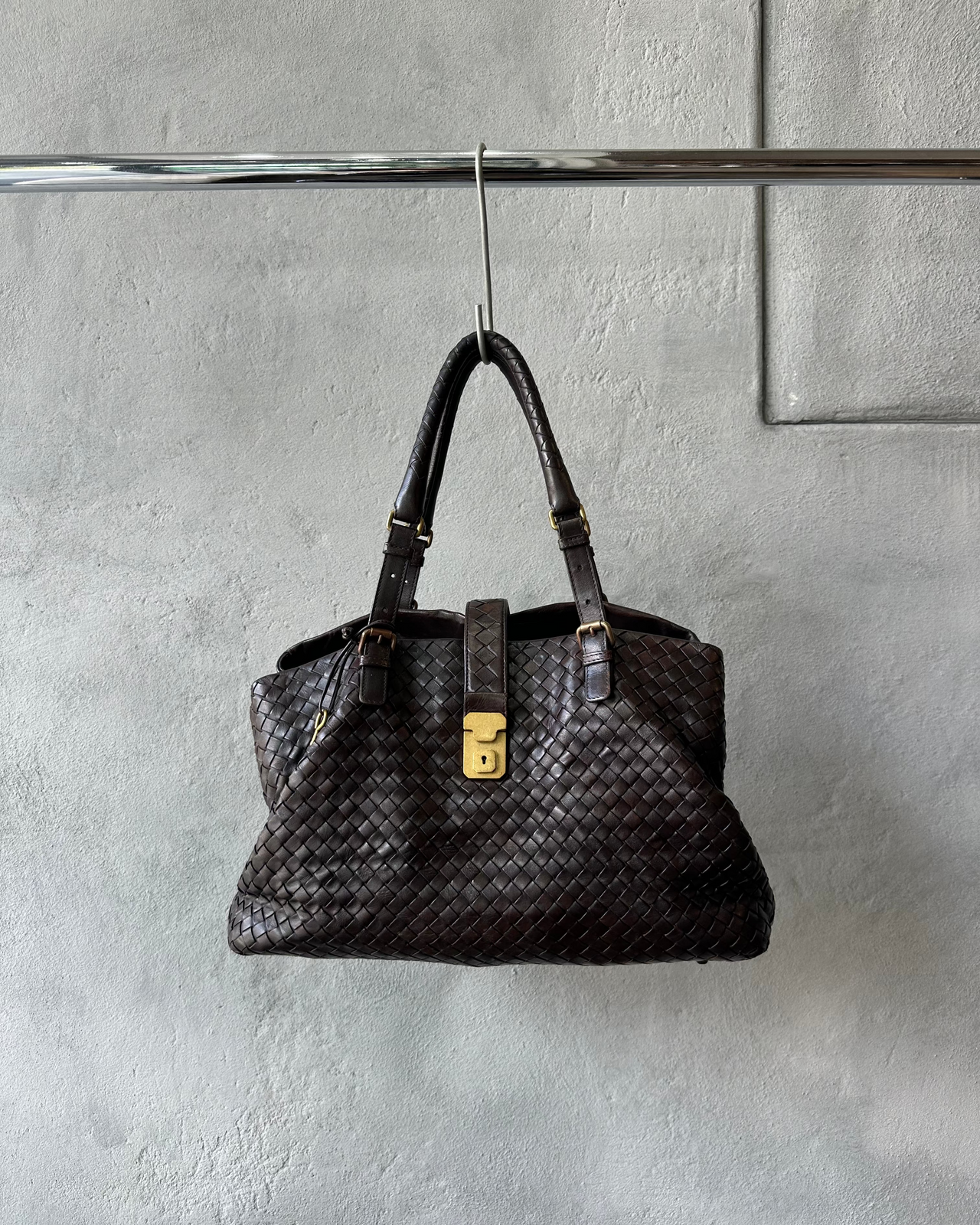 Brown woven Bottega Veneta handbag hanging on a hook against a gray wall