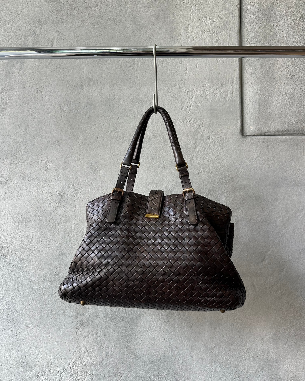 Brown woven Bottega Veneta handbag hanging on a hook against a gray wall