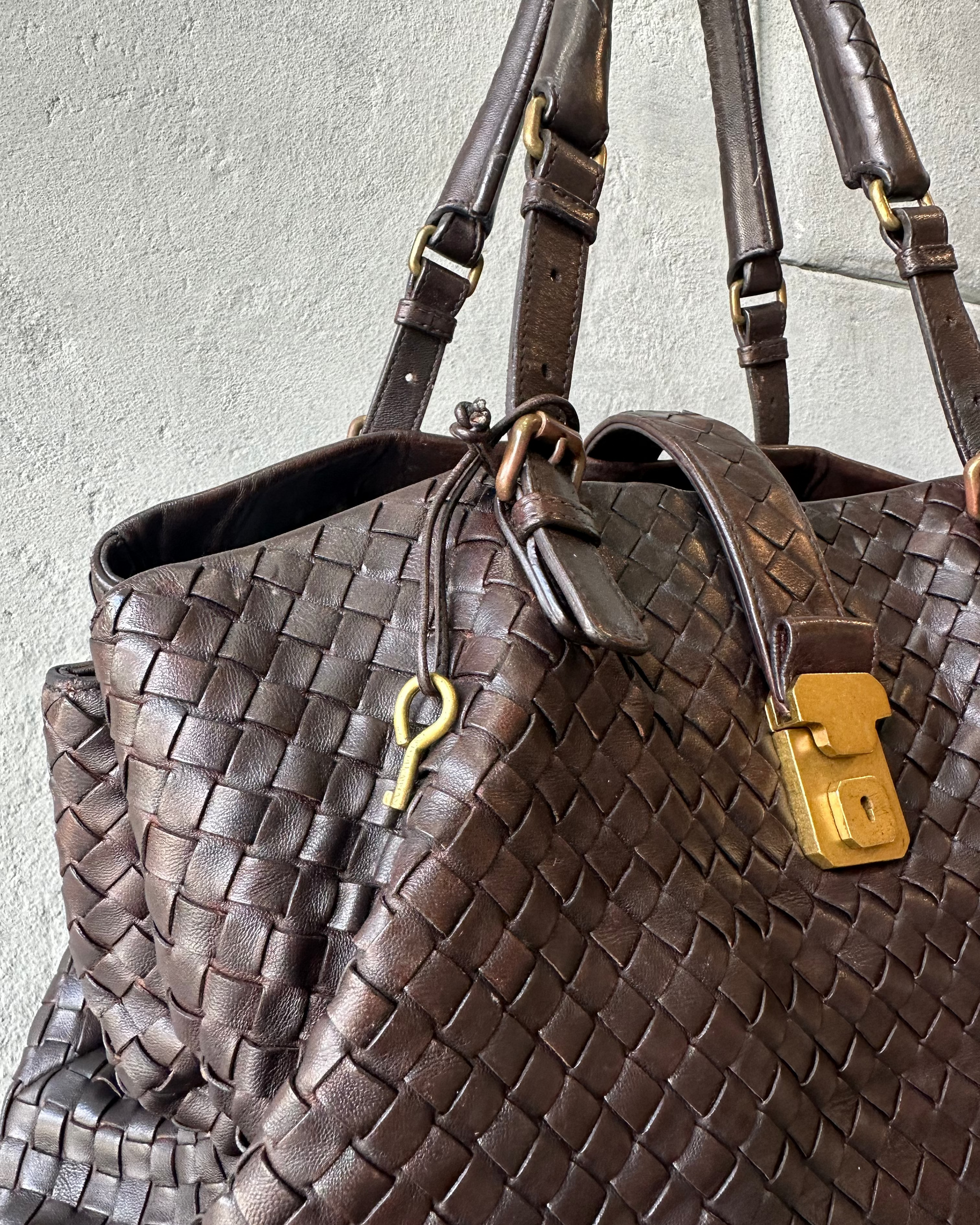 Brown woven Bottega Veneta handbag with gold lock and key on a light gray background