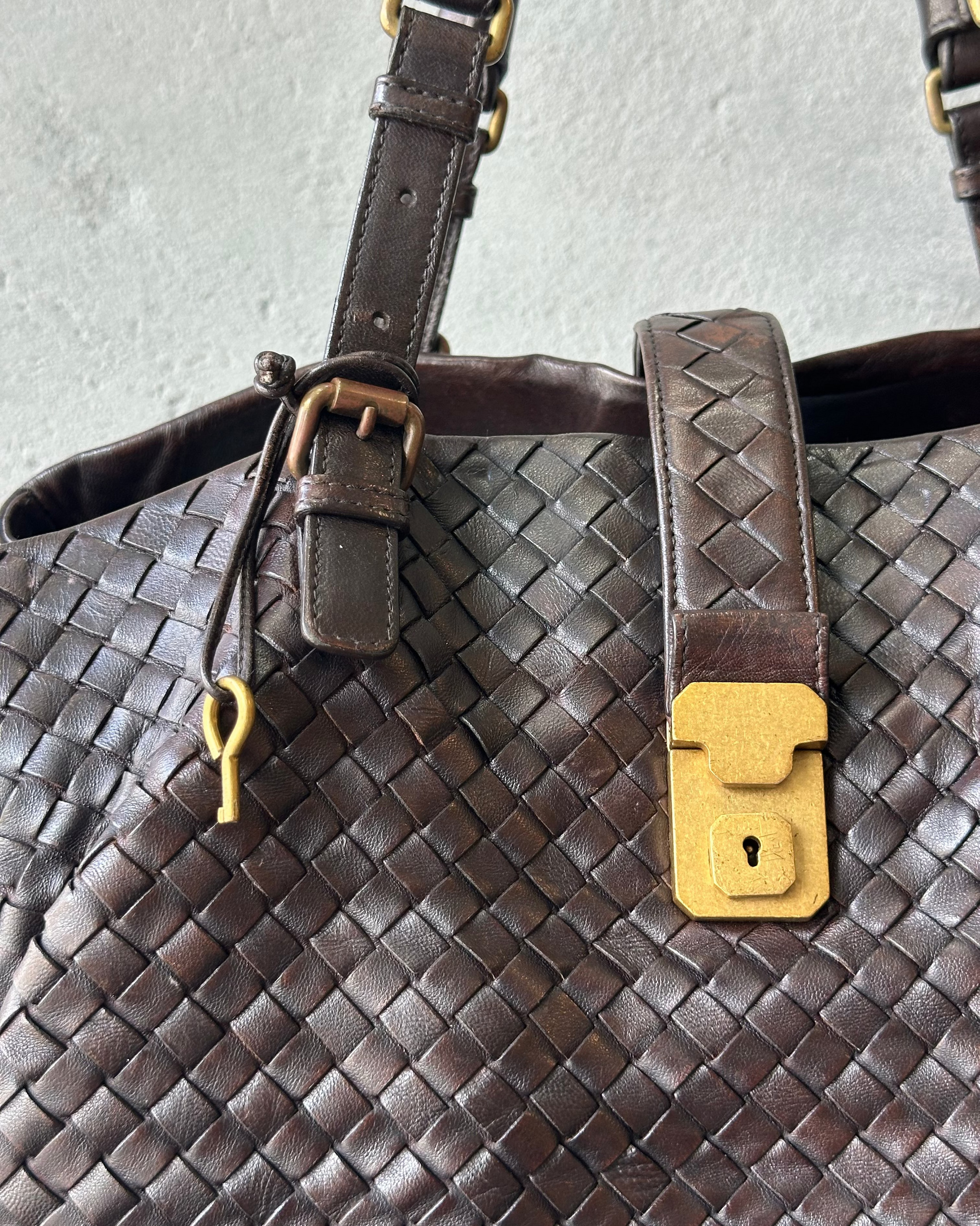 Brown woven leather Bottega Veneta handbag with a yellow lock and key detail on a light gray background