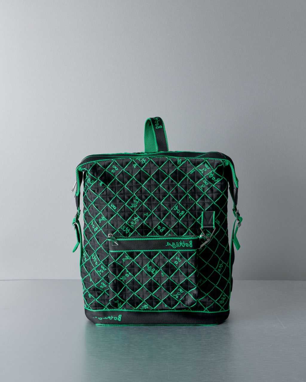 Green and black Bottega Veneta quilted backpack on a gray background