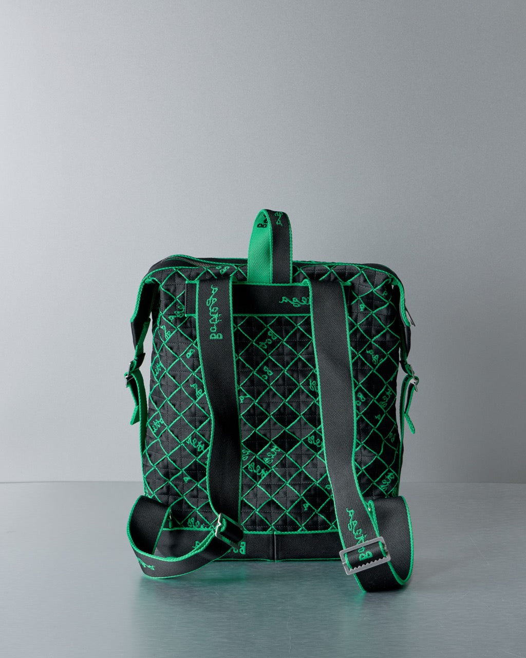 Green and black Bottega Veneta quilted backpack on a gray background