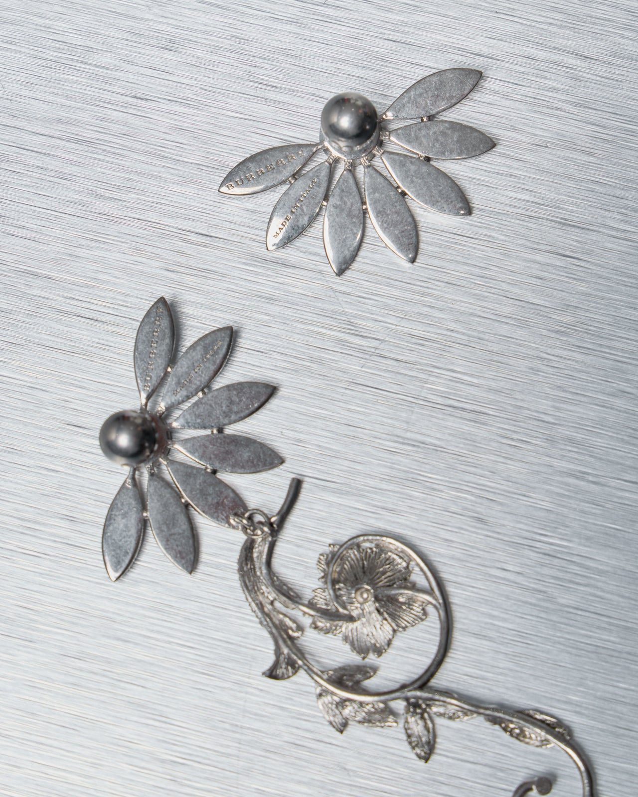 Silver floral Burberry earrings on a textured gray surface