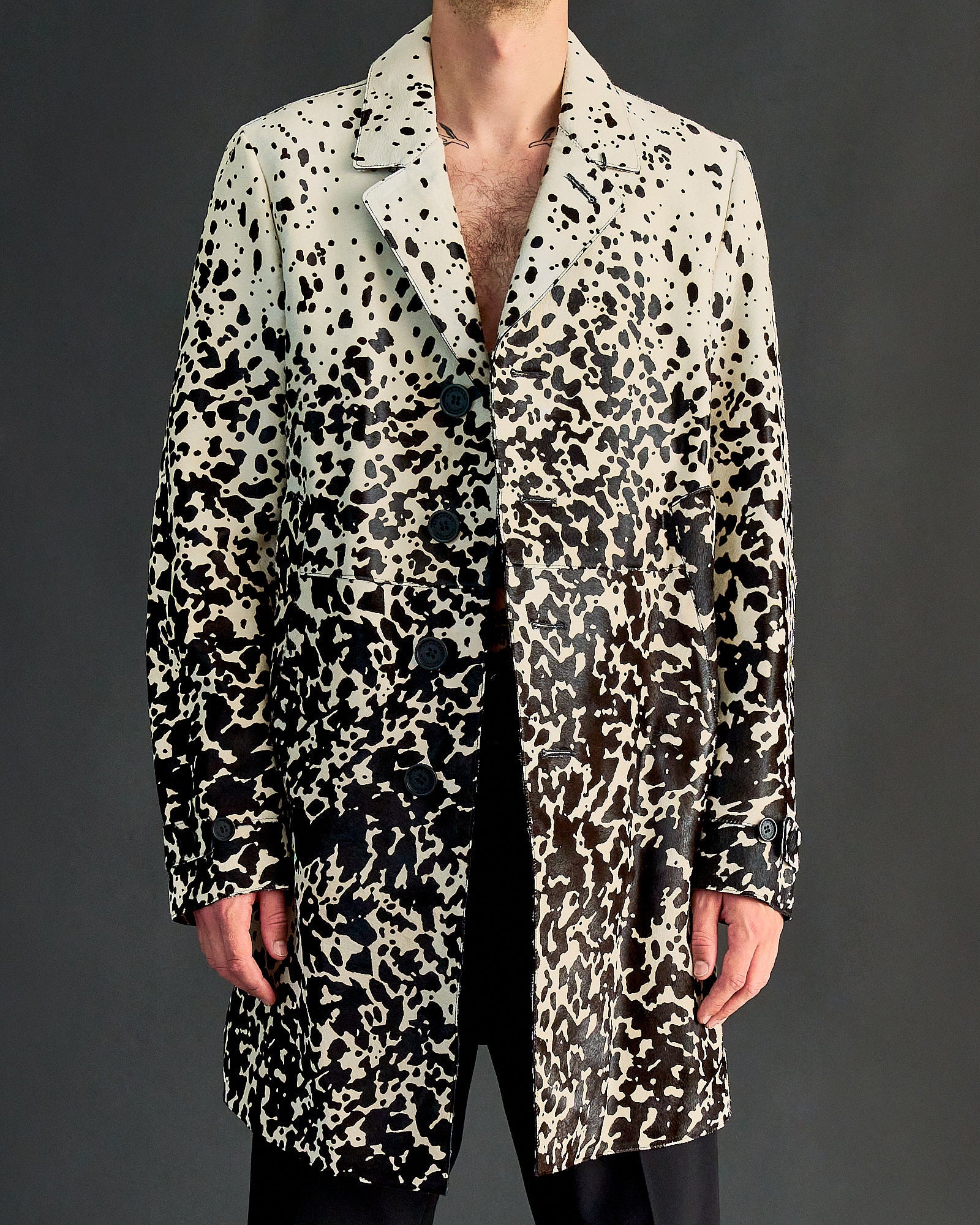 A person wearing a long, black-and-white speckled Burberry coat with a gradient effect. The coat's pattern resembles abstract black splatters.