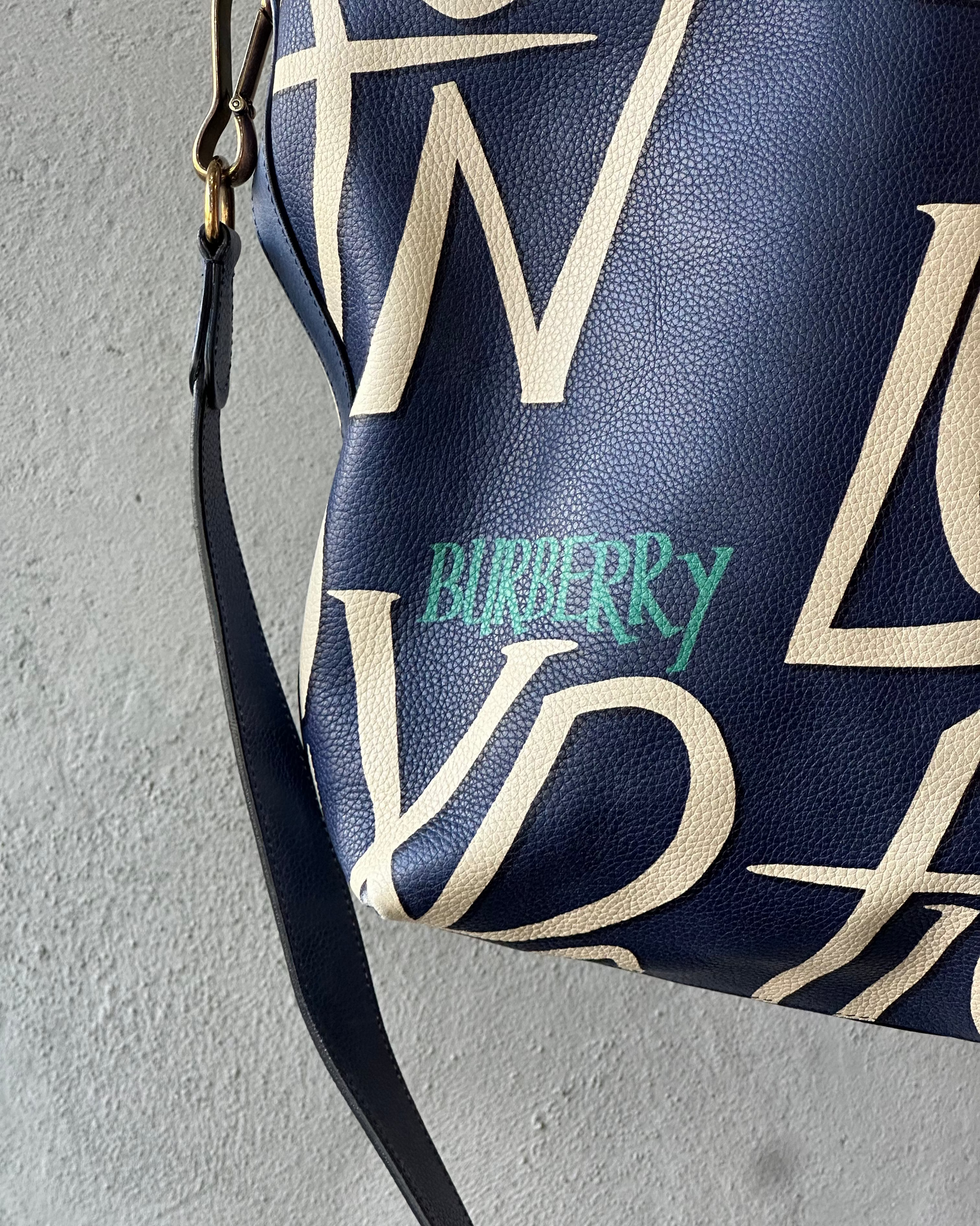 Navy blue handbag with beige geometric pattern and Burberry logo on a gray background