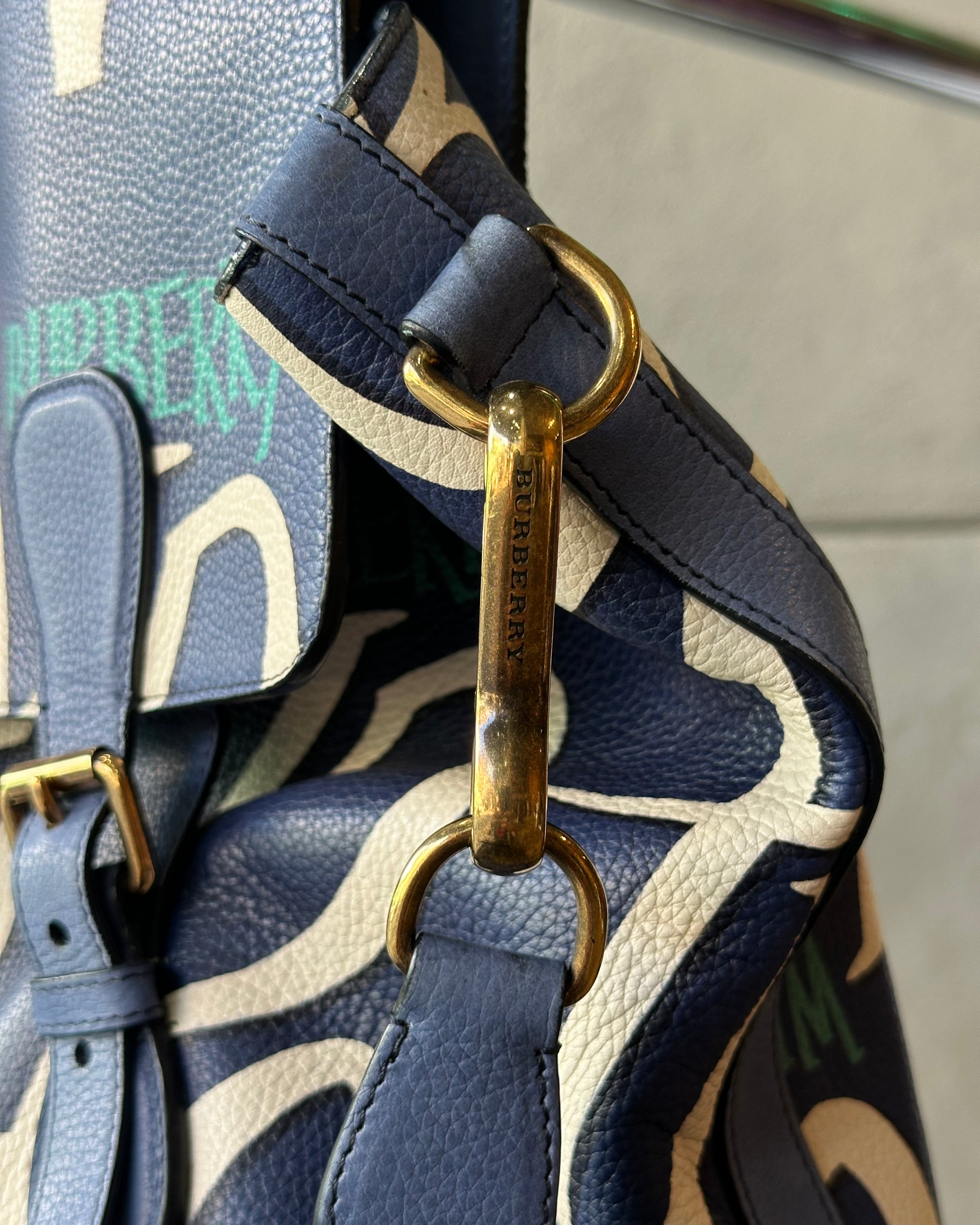 Close-up of a Burberry handbag strap with gold hardware on a patterned background