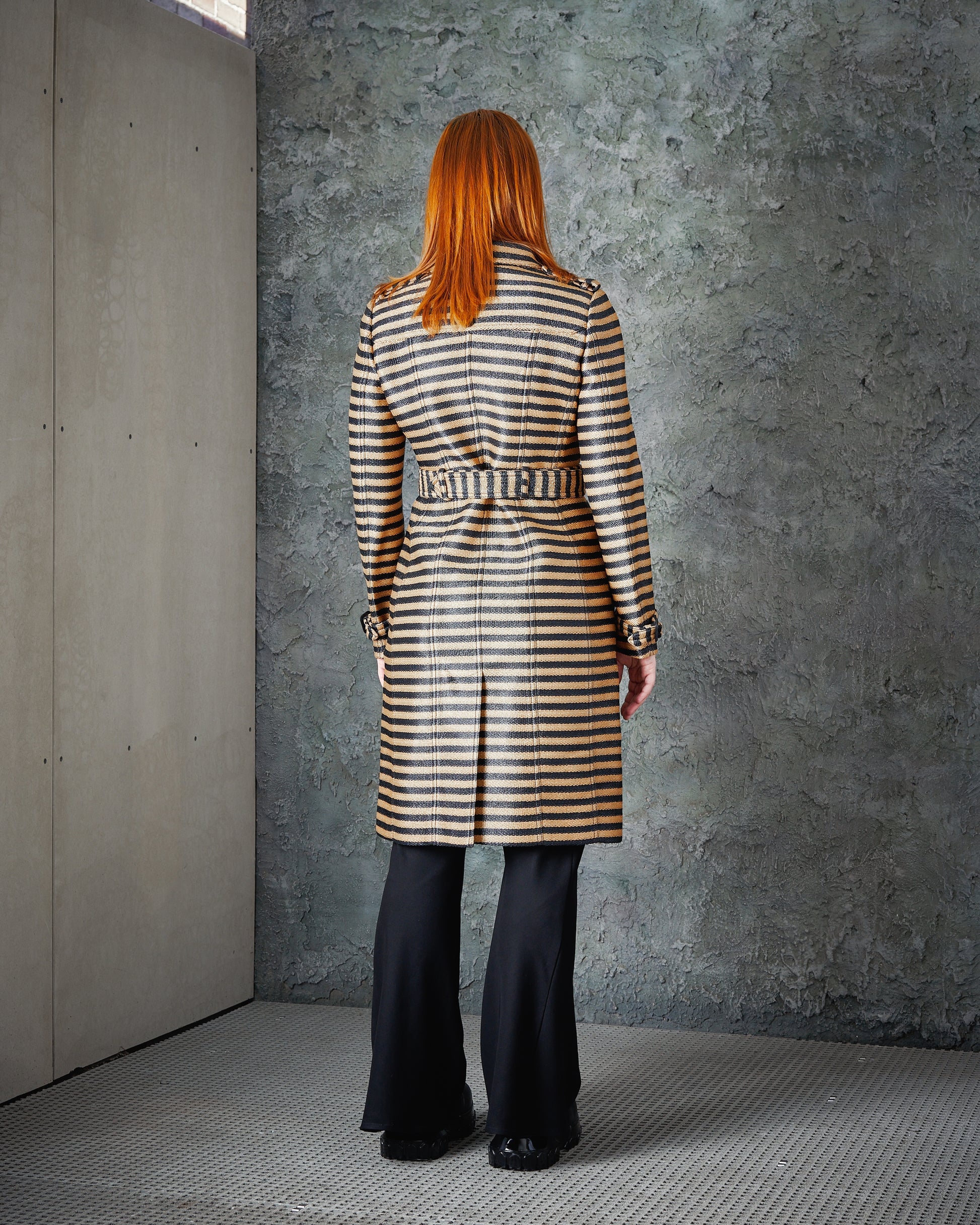 A person wears a striped Burberry coat and black flared pants.