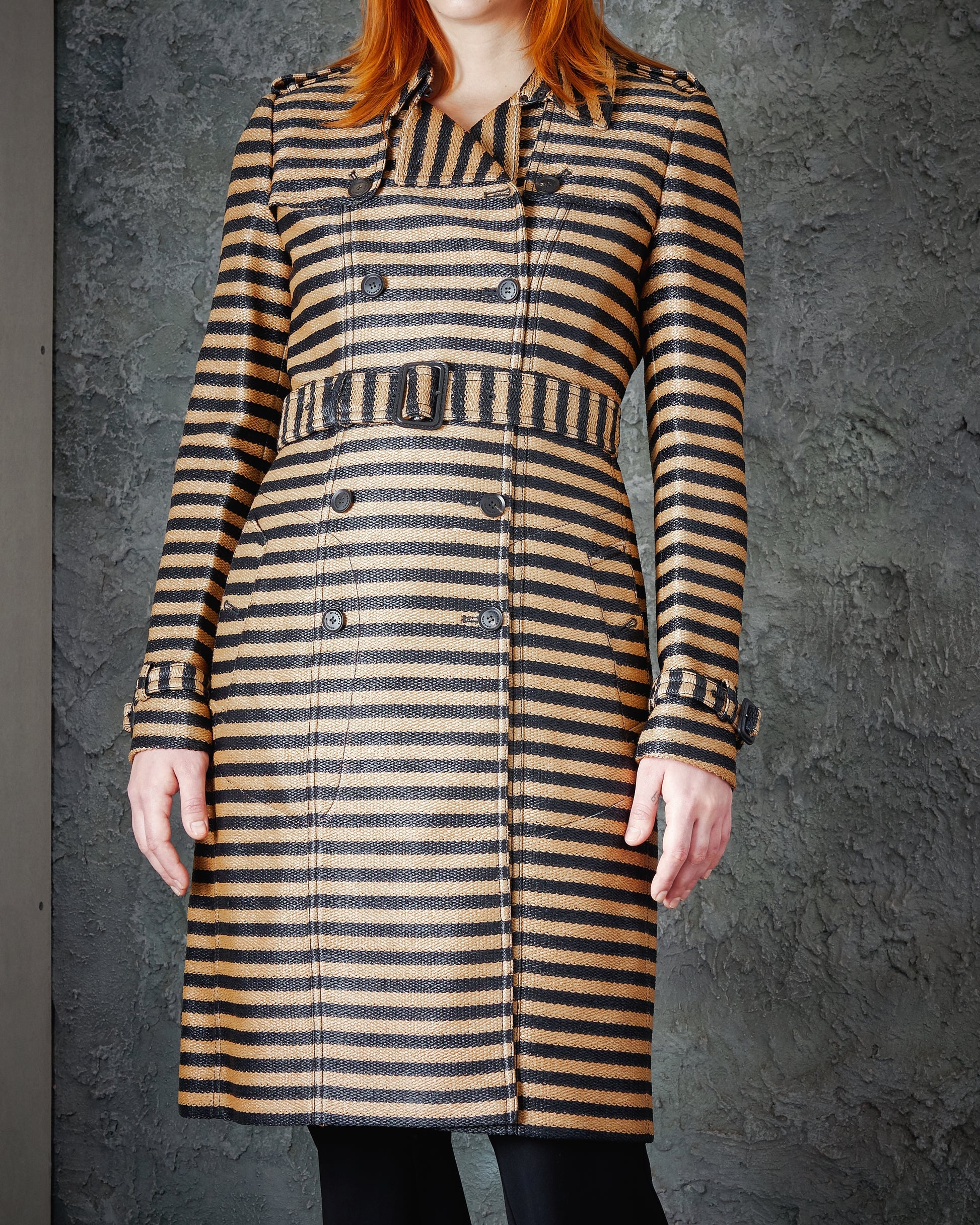 A person wearing a knee-length, double-breasted, striped Burberry coat with brown and black horizontal lines.