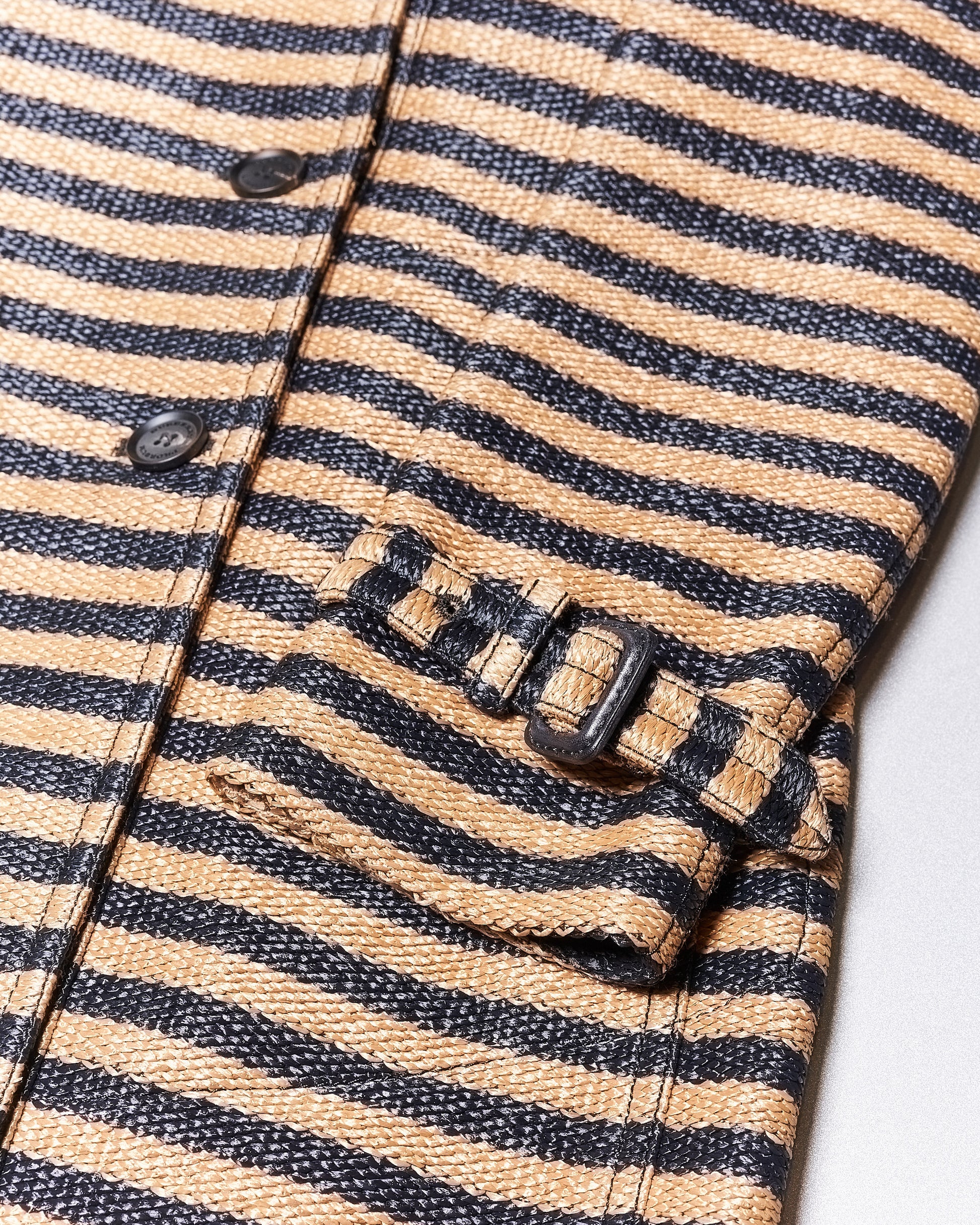 Close-up of a beige and black striped Burberry coat sleeve with button details. The pattern is bold, and the fabric has a textured appearance.