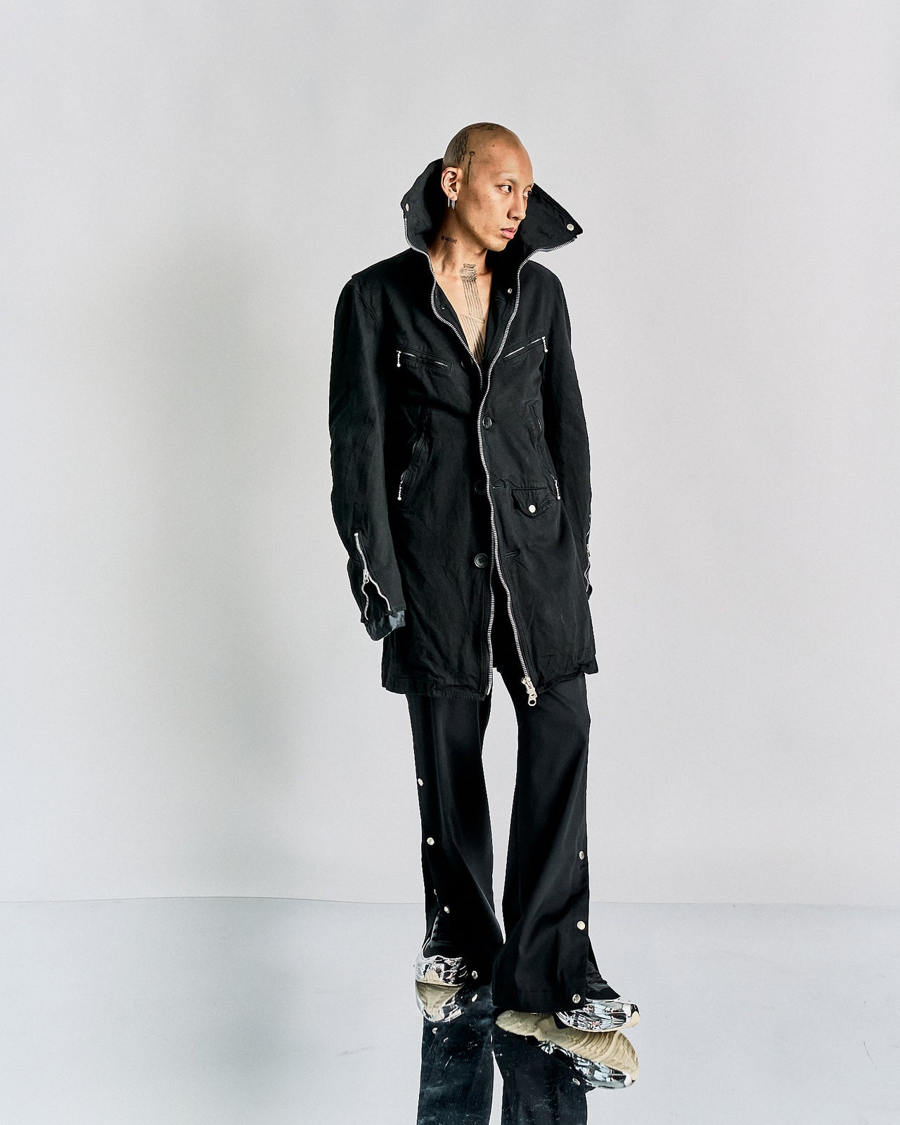 A black longline CDG Junya Watanabe front-zip jacket with collar, featuring external zip and press-stud pockets, and polished hardware.