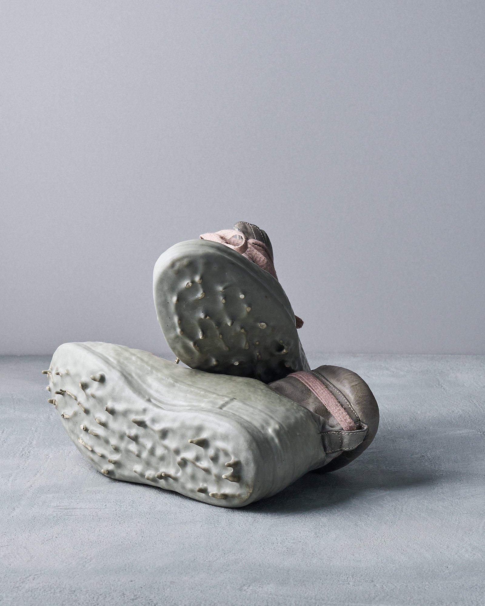 Close-up of two rugged shoes with chunky, textured Carol Christian Poell soles against a neutral background. The soles have a unique, artistic wavy design, conveying creativity.