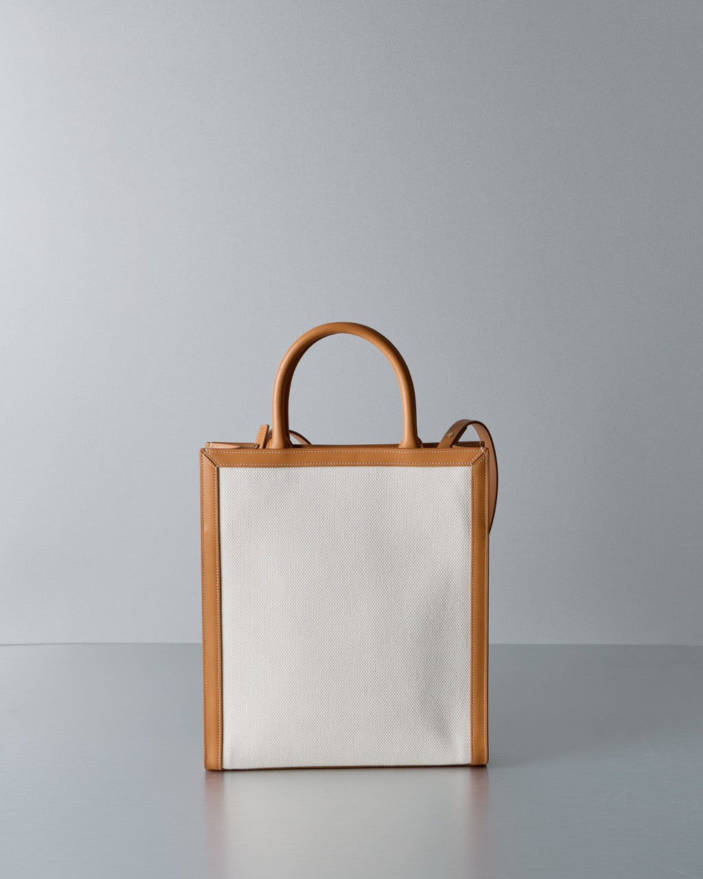 Celine tote bag with brown leather handles and trim on a gray background