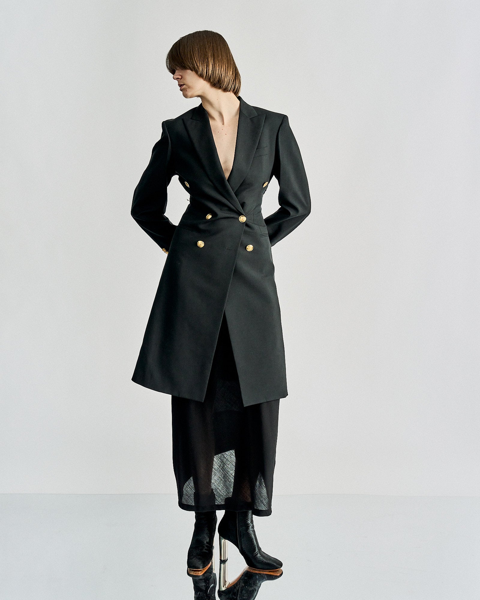 A person wearing a tailored black Celine blazer dress with gold buttons, conveying a formal and elegant tone. The background is neutral grey.