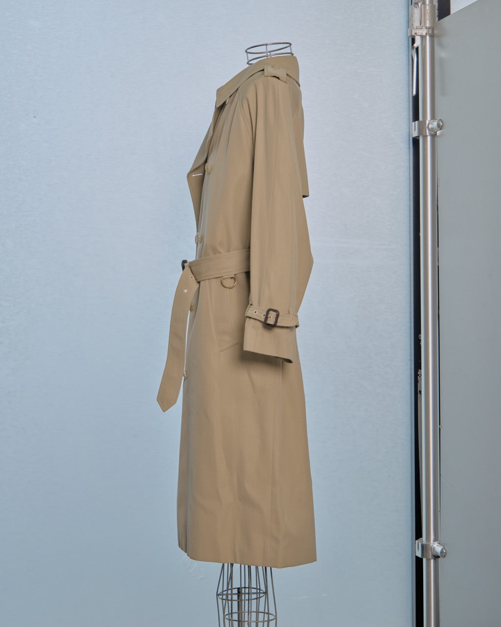 Beige Celine trench coat on a mannequin against a light blue wall.