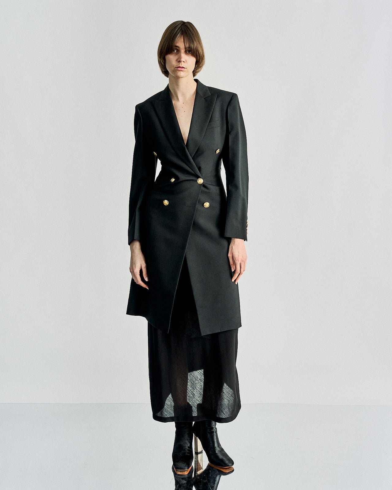 A person wearing a sleek, black double-breasted Celine coat with gold buttons over a long, sheer black skirt and boots, creating a chic, modern look.