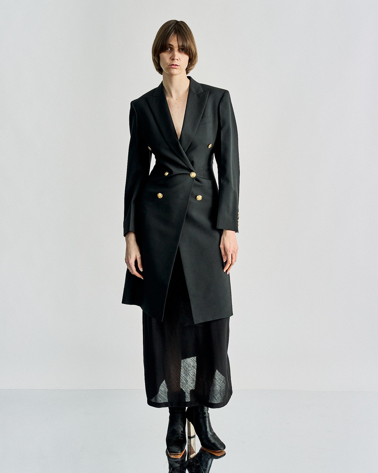 A person wearing a sleek, black double-breasted Celine coat with gold buttons over a long, sheer black skirt and boots, creating a chic, modern look.