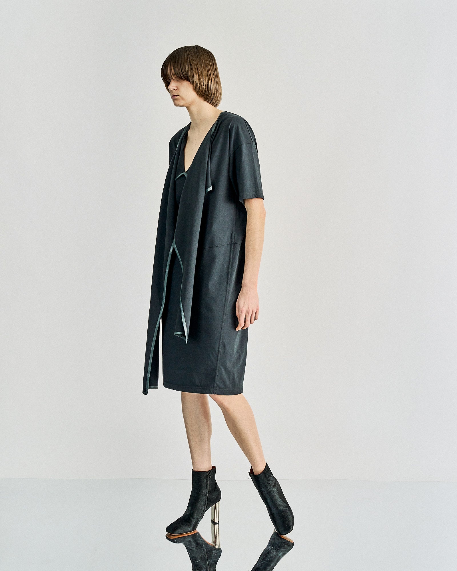A person with short hair wears a dark gray, draped Celine dress with short sleeves, paired with ankle-high black boots. 
