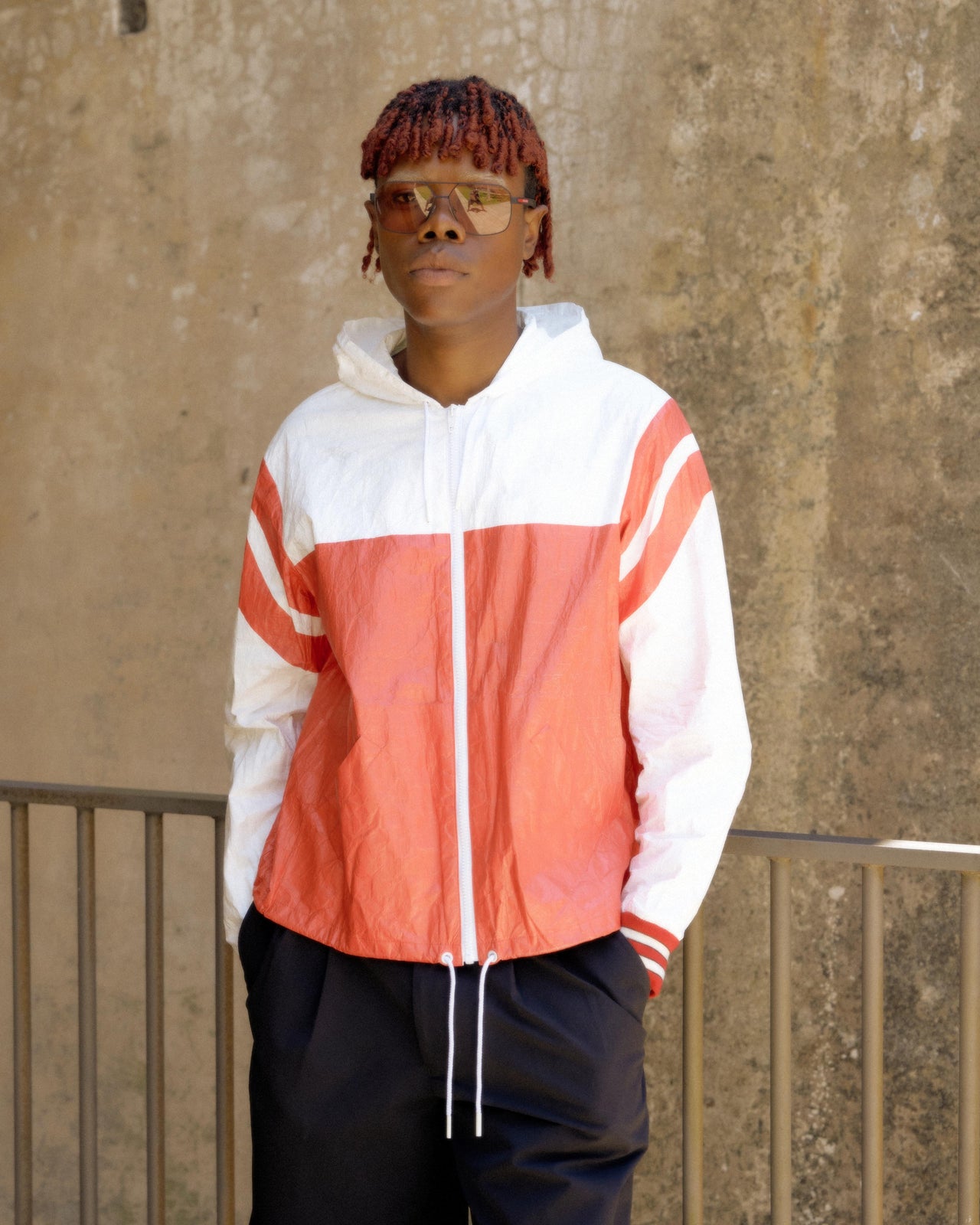 A person wearing a red, white, and black striped hooded Celine windbreaker jacket and black pants.
