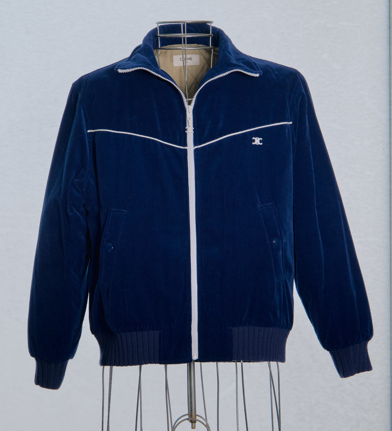 Navy blue Celine jacket with white zipper on a mannequin against a light gray background