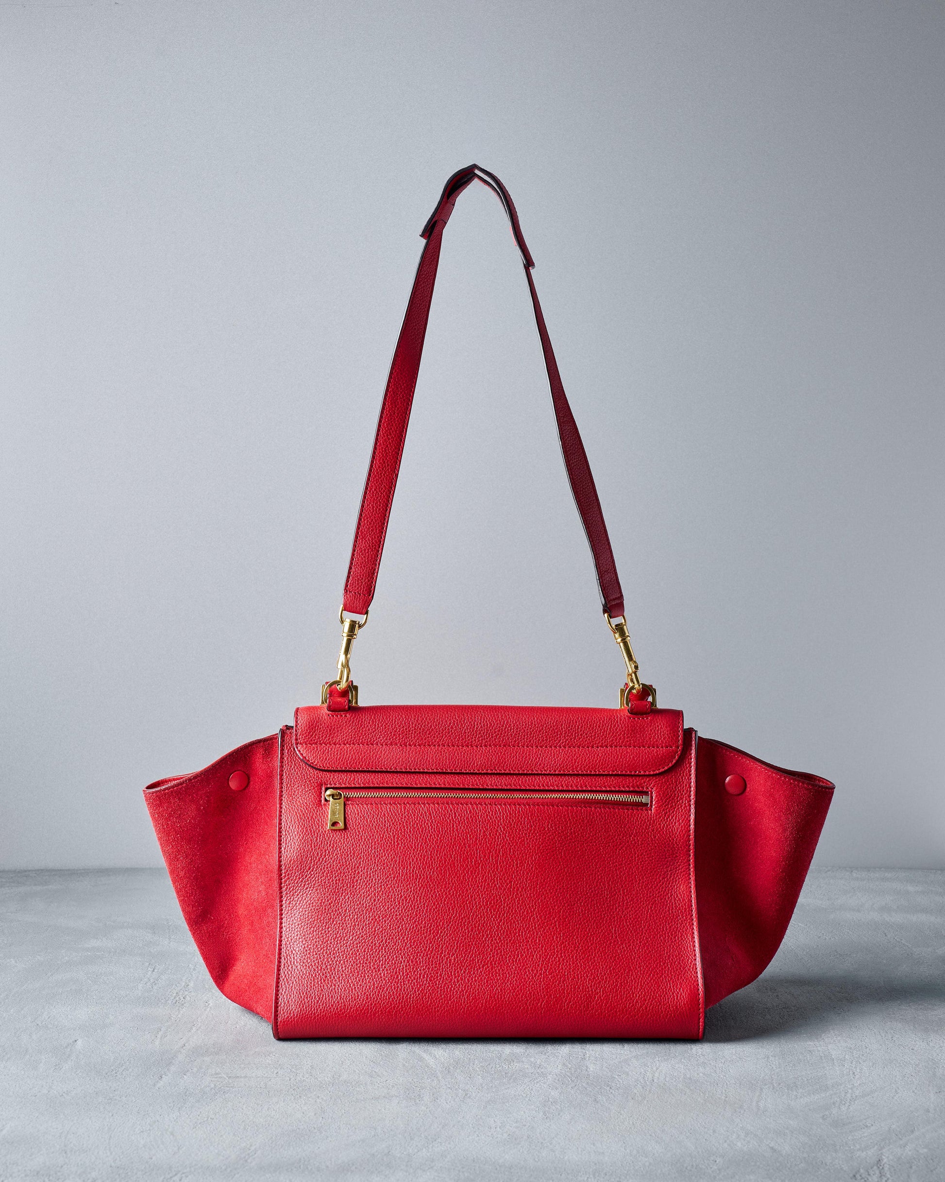 Reverse of a red Celine suede medium trapeze bag with a removable strap, featuring a main zip compartment and expandable side panels.