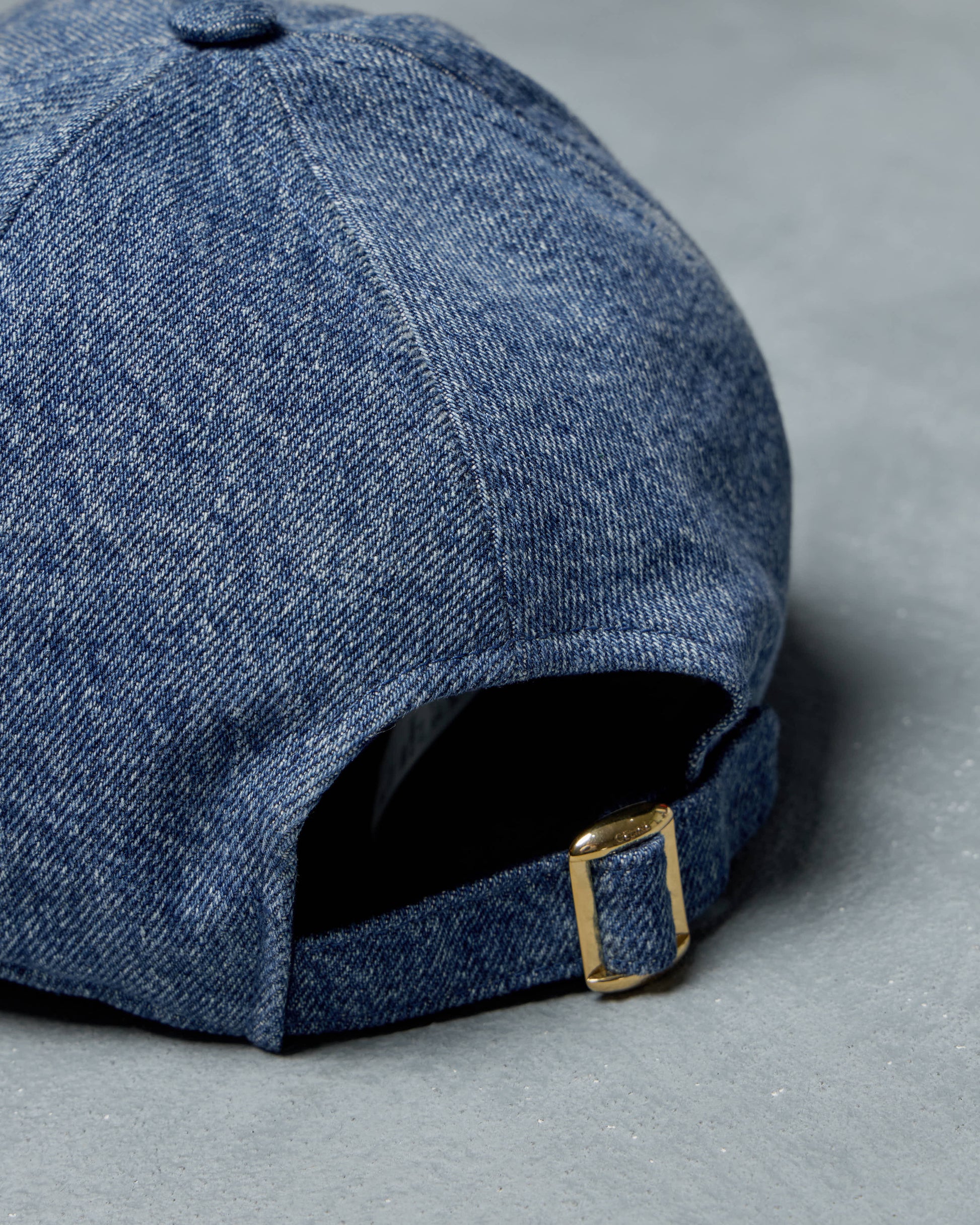 Blue denim Celine cap with a gold buckle on a gray background
