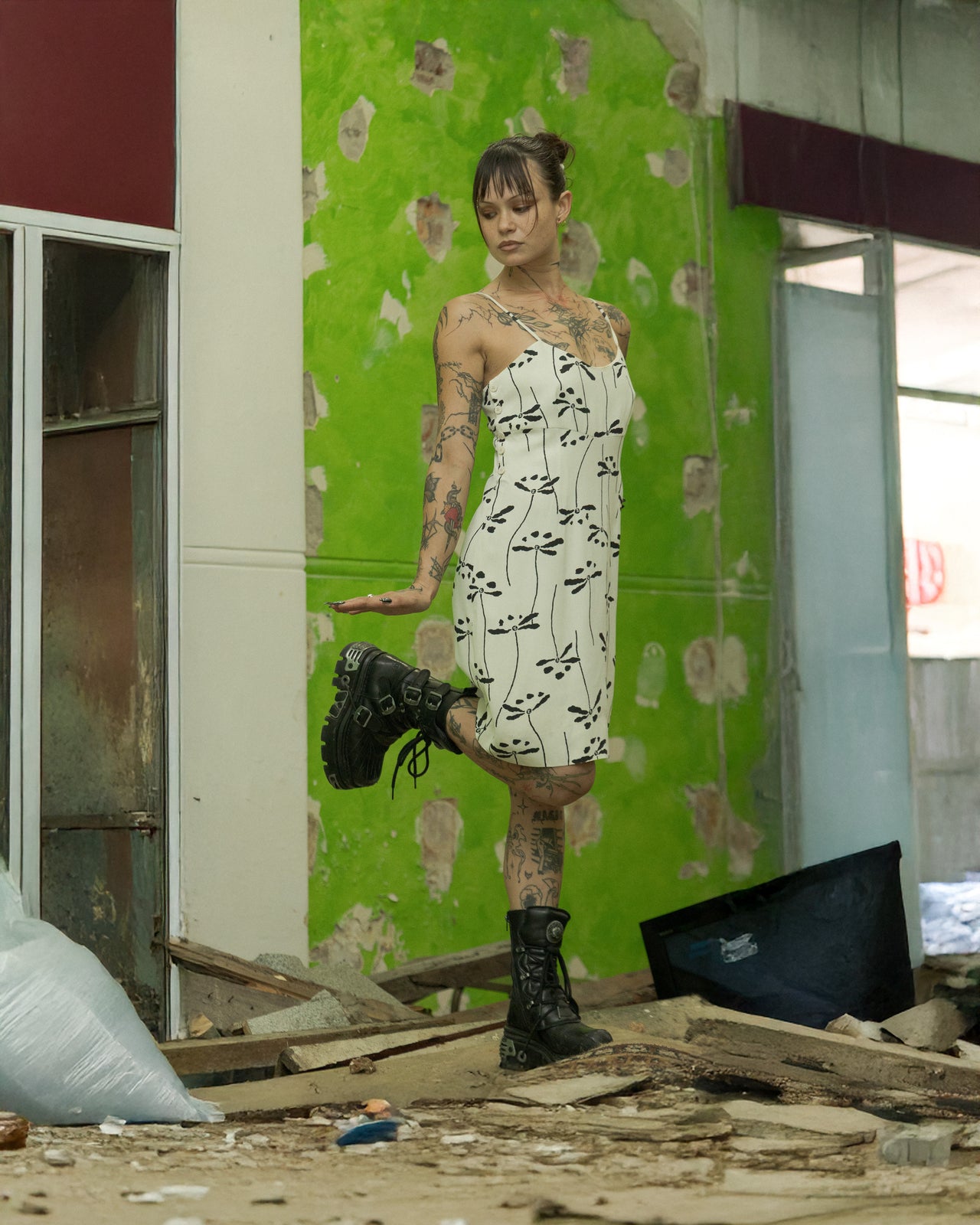 A person standing in a dilapidated room wearing a floral print mini Chanel dress with a hidden back zip and hook closure.