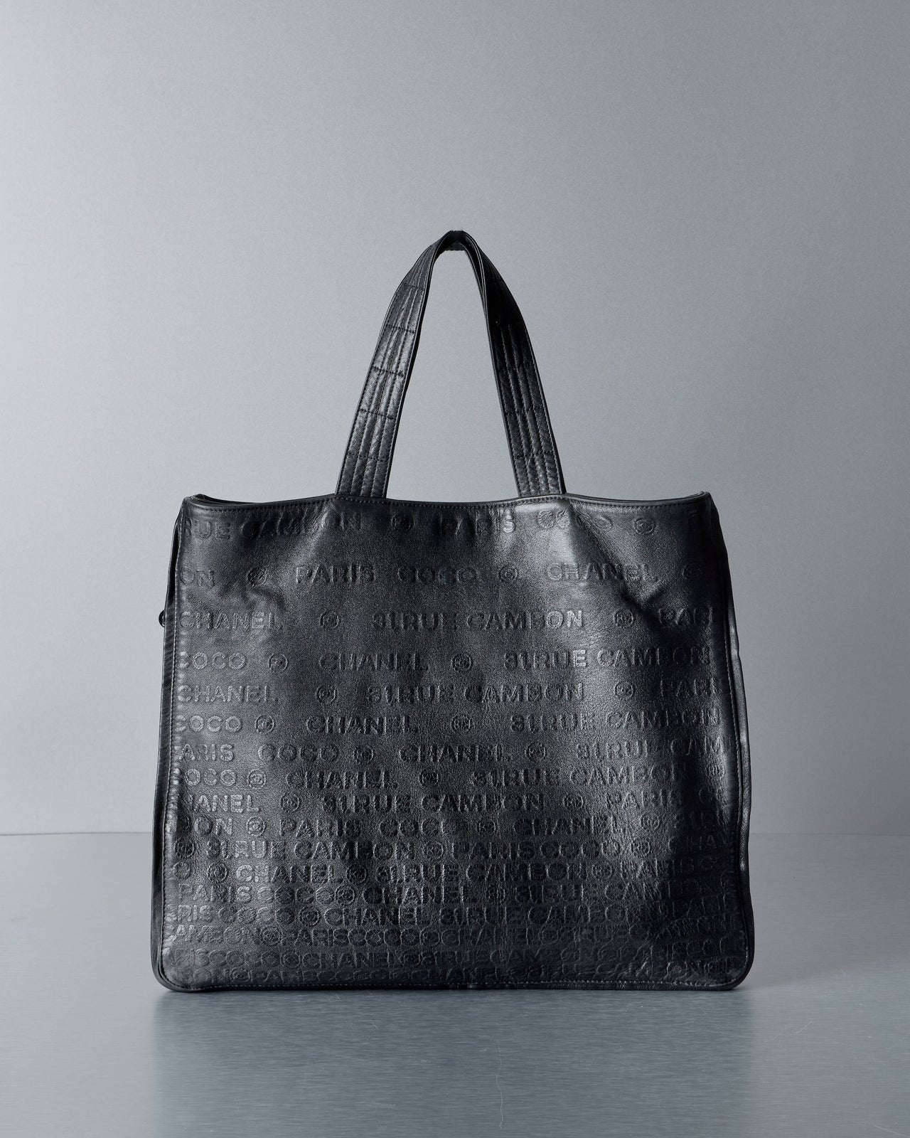 Black textured Chanel tote bag on a gray background