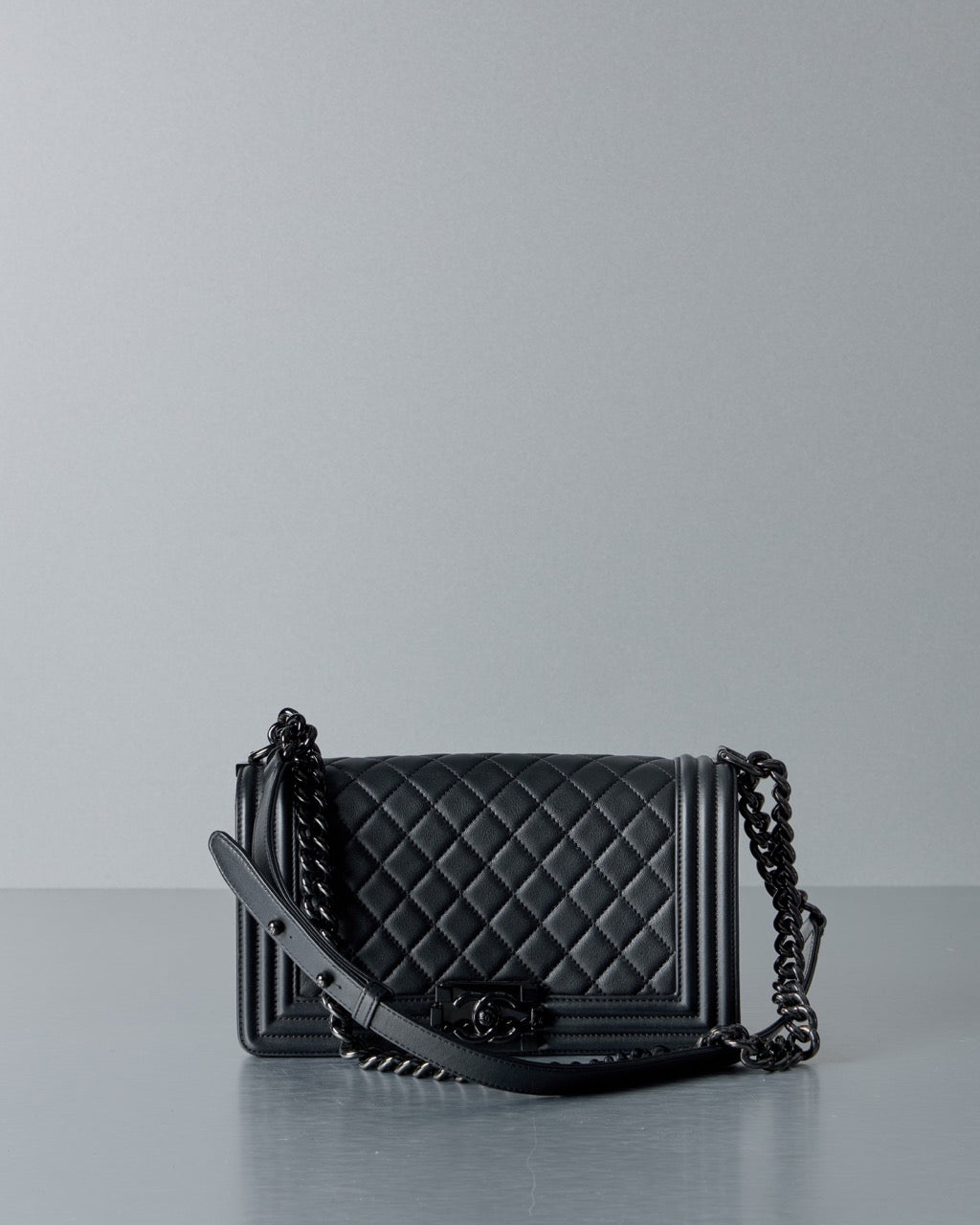 Black quilted Chanel handbag with chain strap on a gray background