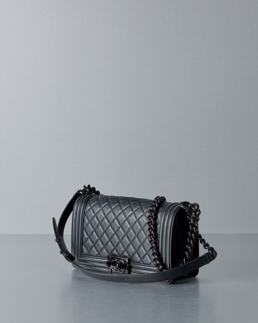 Quilted black Chanel handbag with black chain strap on a light gray background