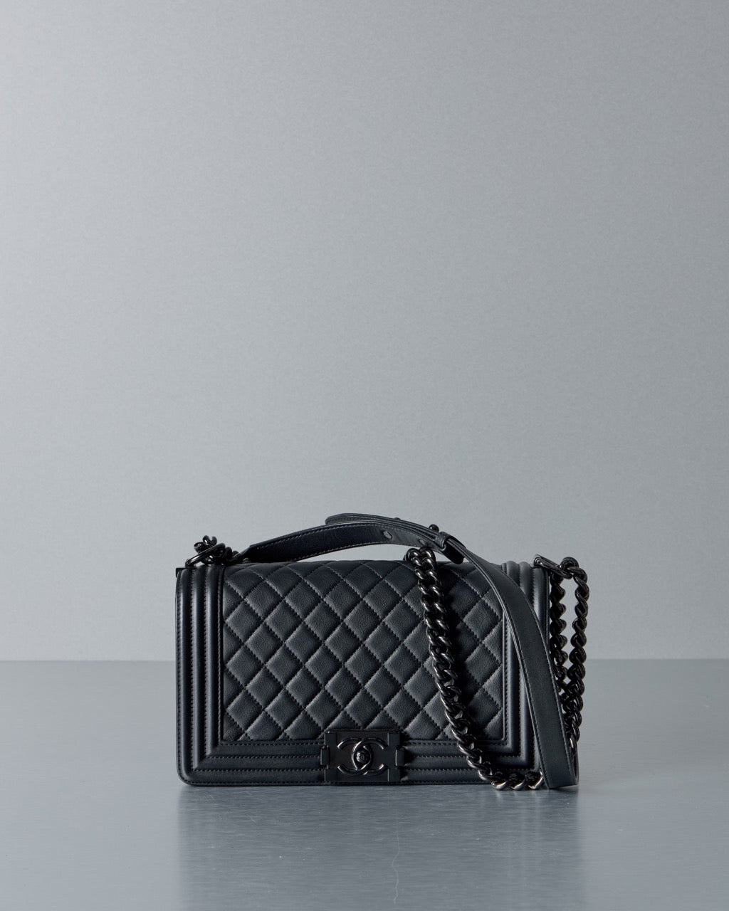 Black quilted Chanel handbag with chain detail on a gray background