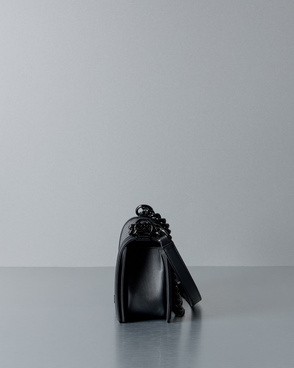 Black Chanel leather handbag on a reflective surface with a light gray background