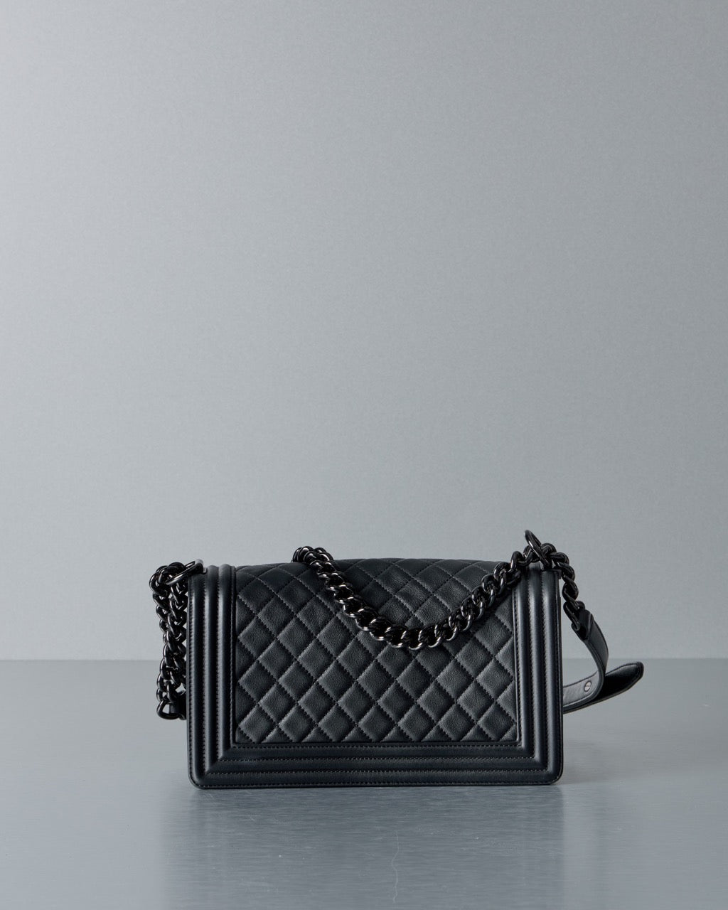 Black Chanel quilted handbag with chain detail on a gray background