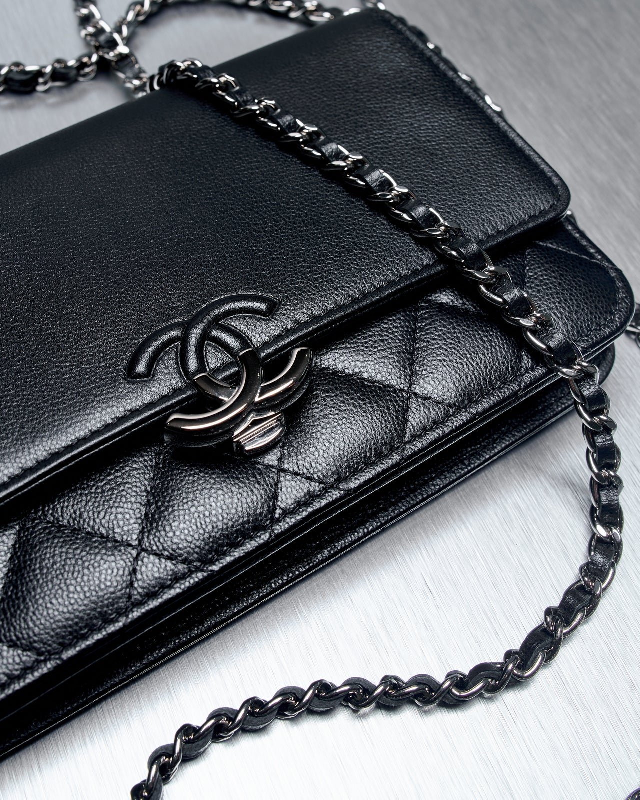 Close-up of a black leather Chanel quilted purse with a silver chain strap and a distinct interlocking CC logo, set on a metal surface. 