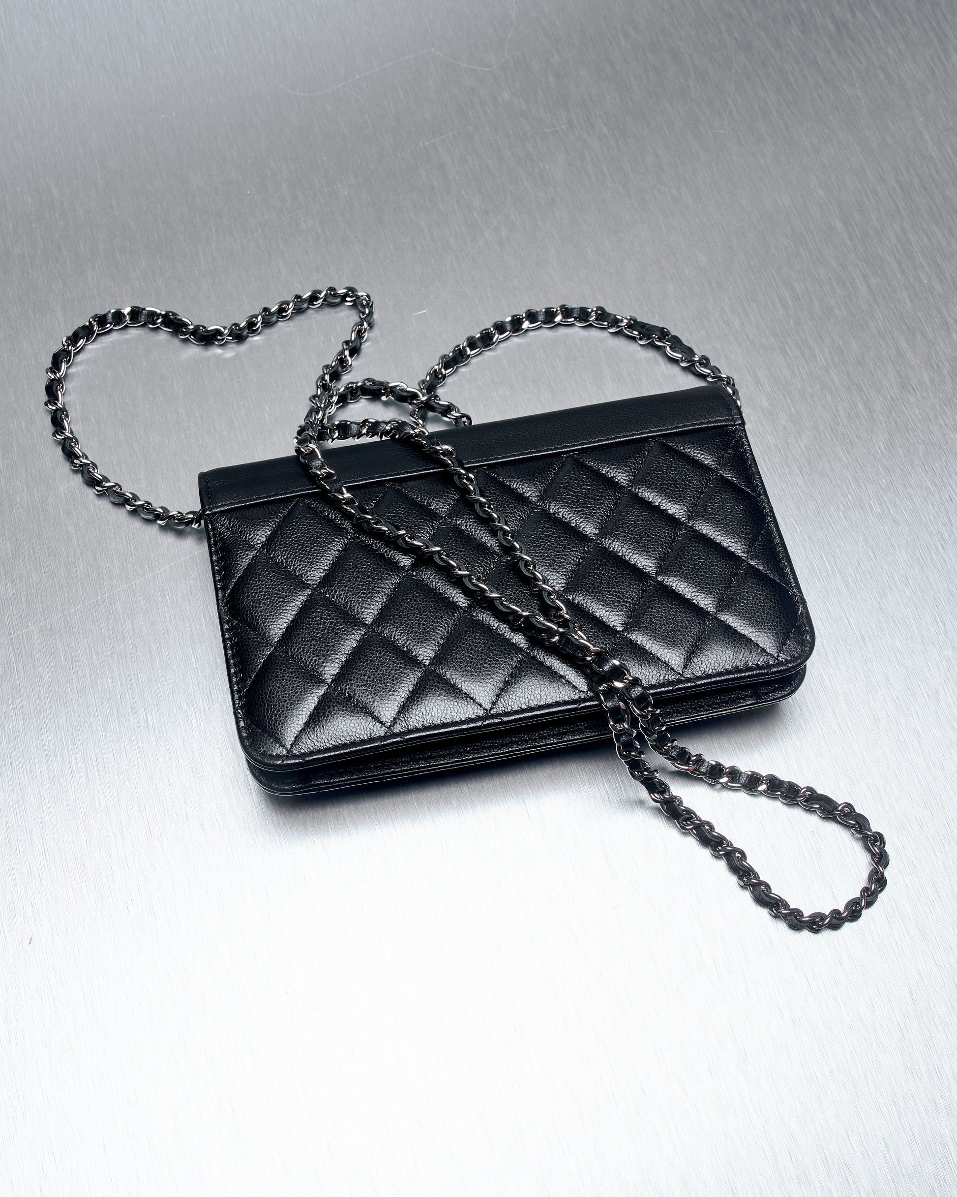 Quilted black leather Chanel bag with a silver chain strap on a metallic textured surface