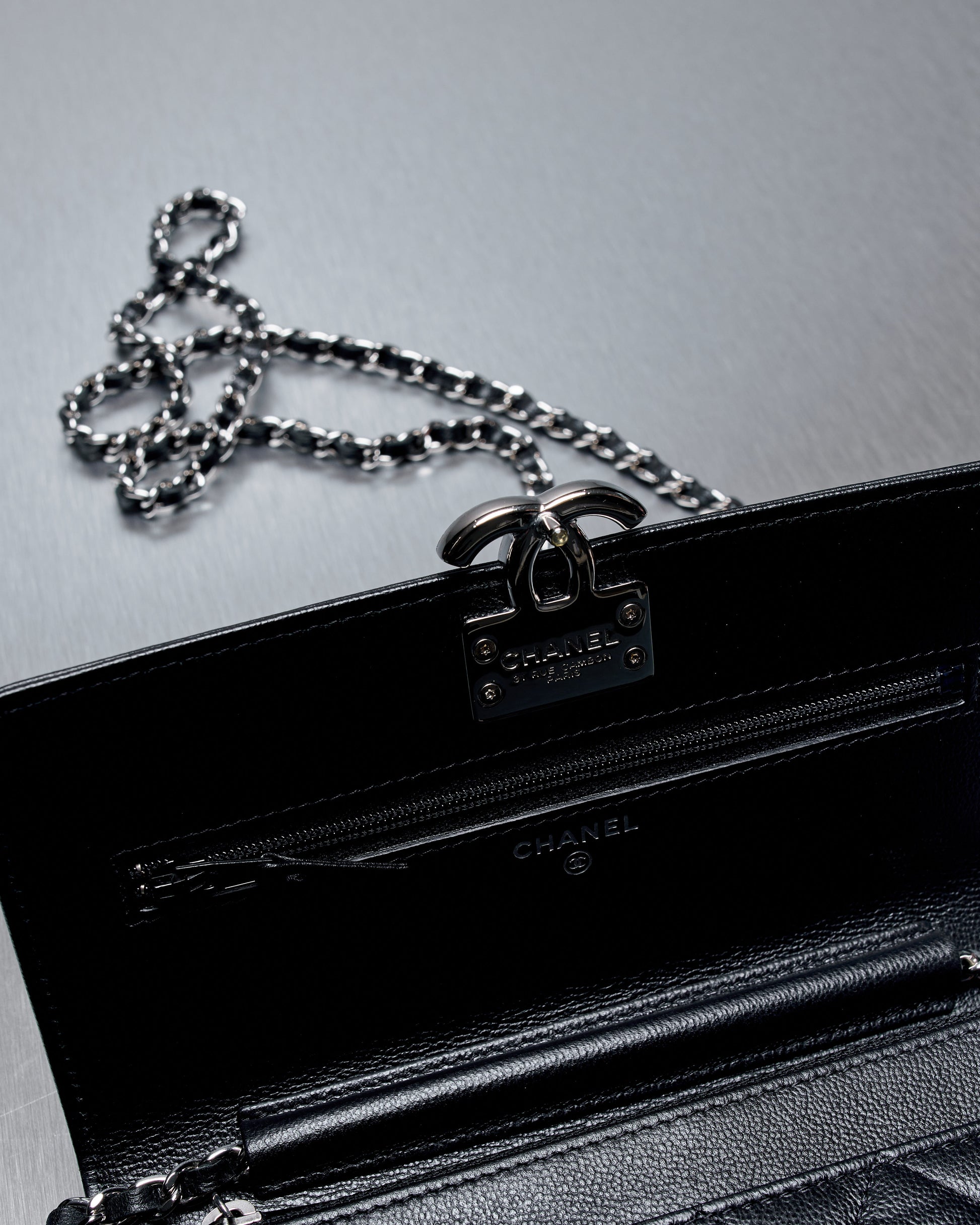A black Chanel handbag with a silver chain strap and metal clasp is opened to reveal interior pockets.