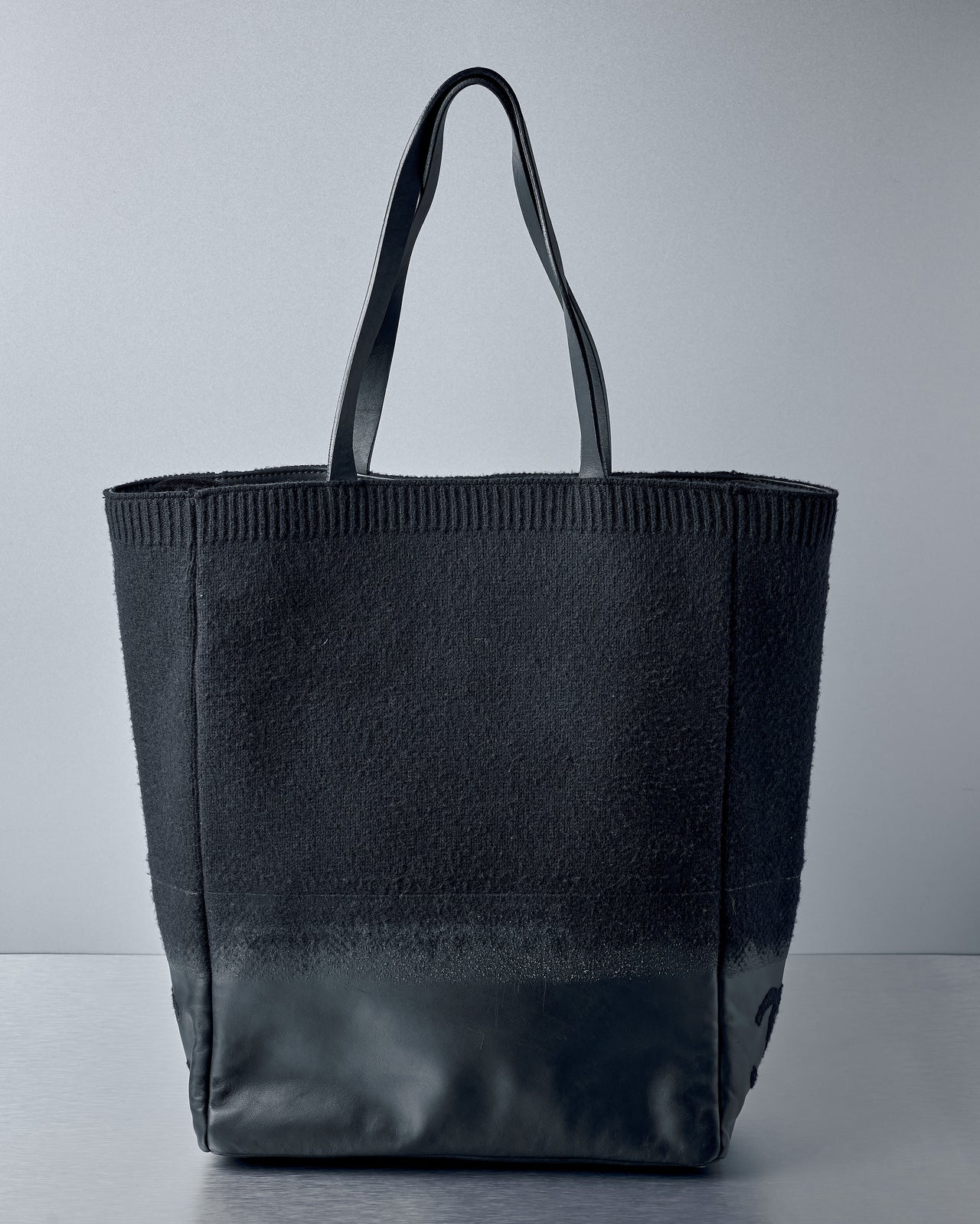 Black Chanel tote bag on a grey background