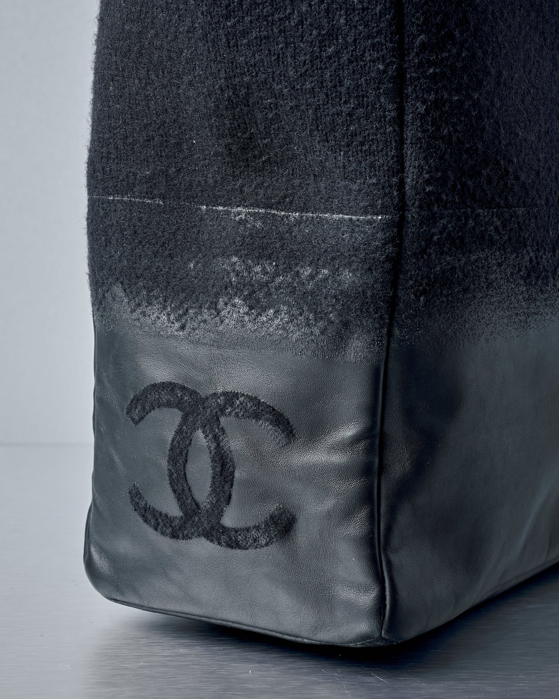 Close-up of a black Chanel bag with logo on a grey background