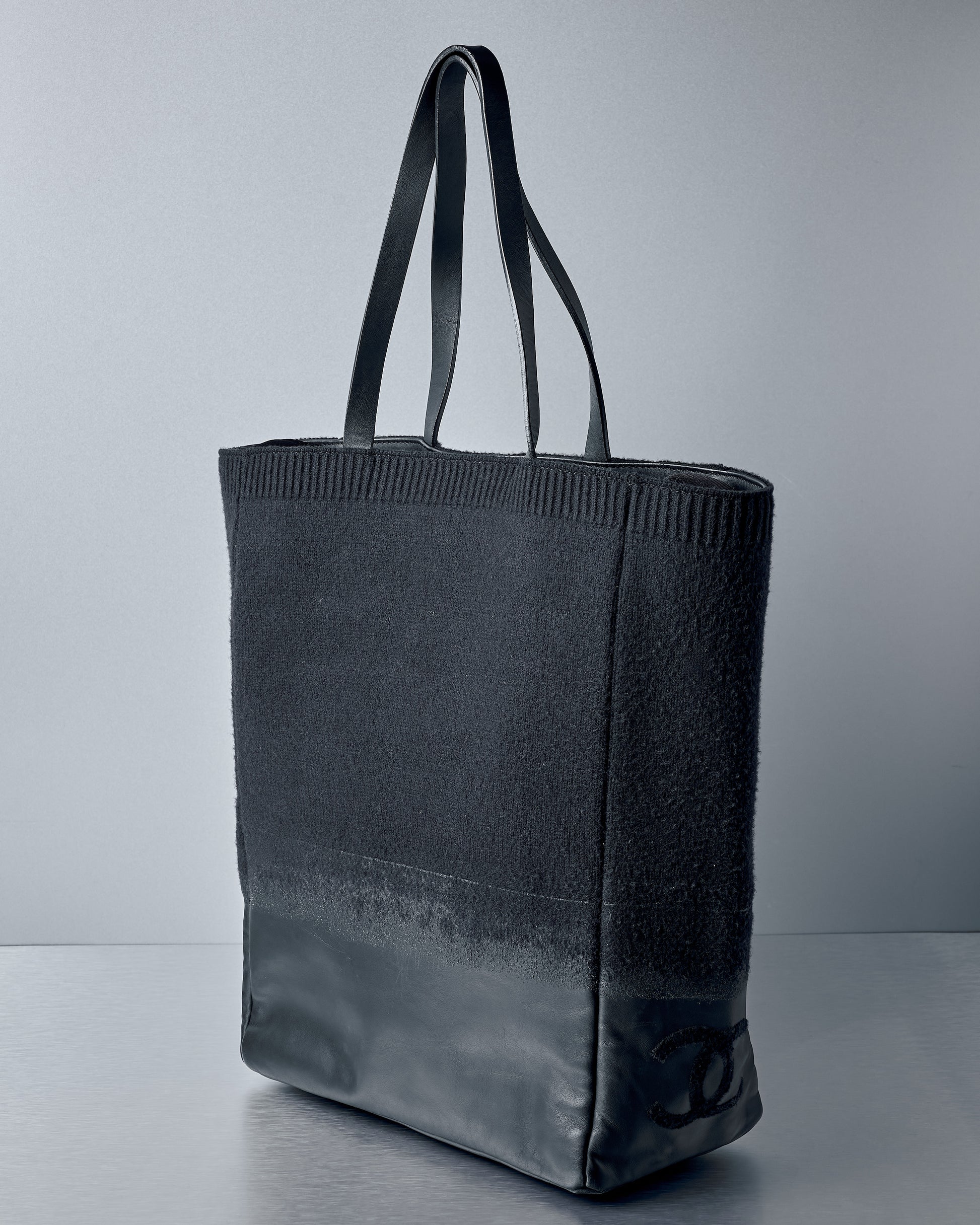 Black textured Chanel tote bag on a grey background