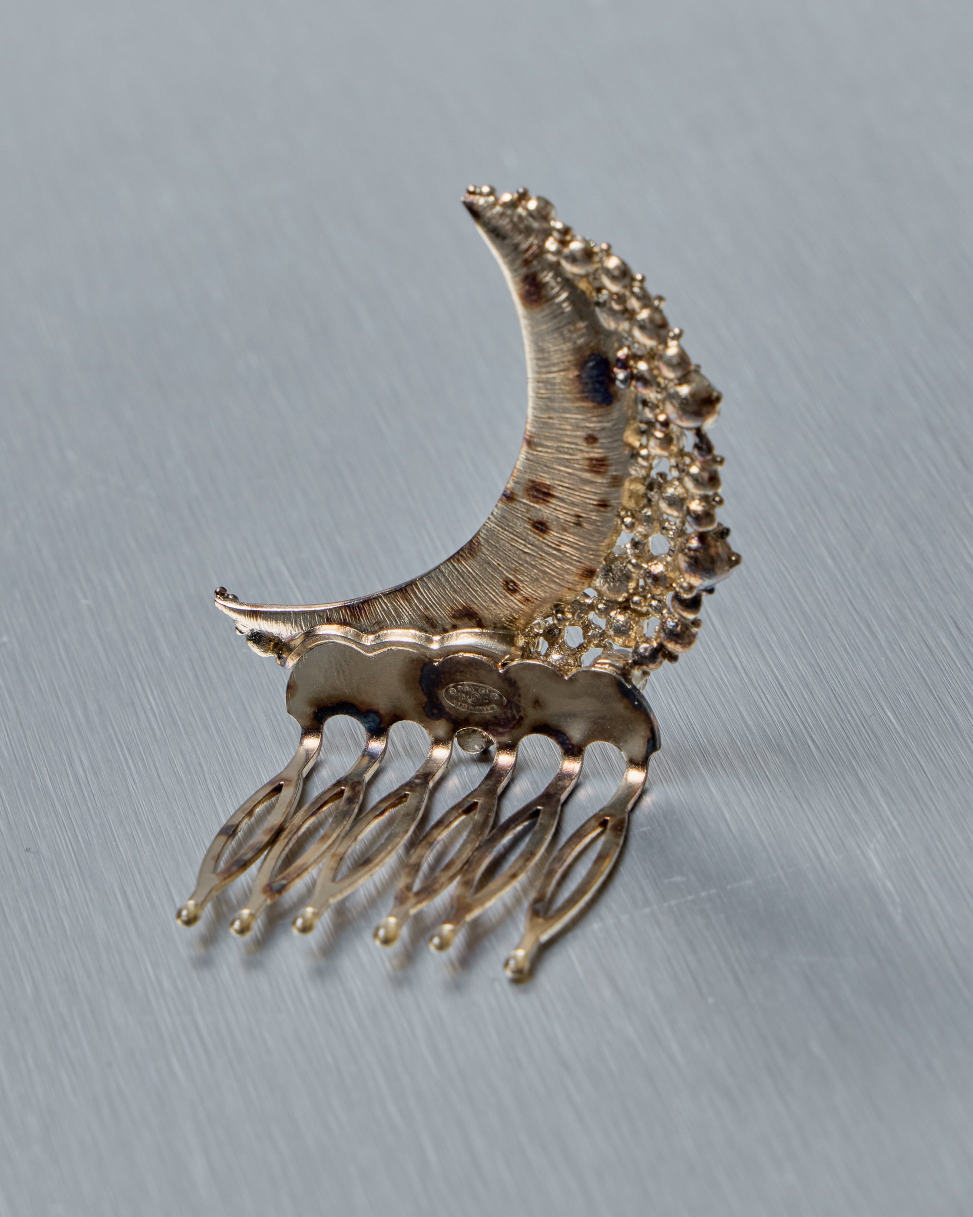 Silver Chanel crescent moon hair comb with decorative elements on a gray background