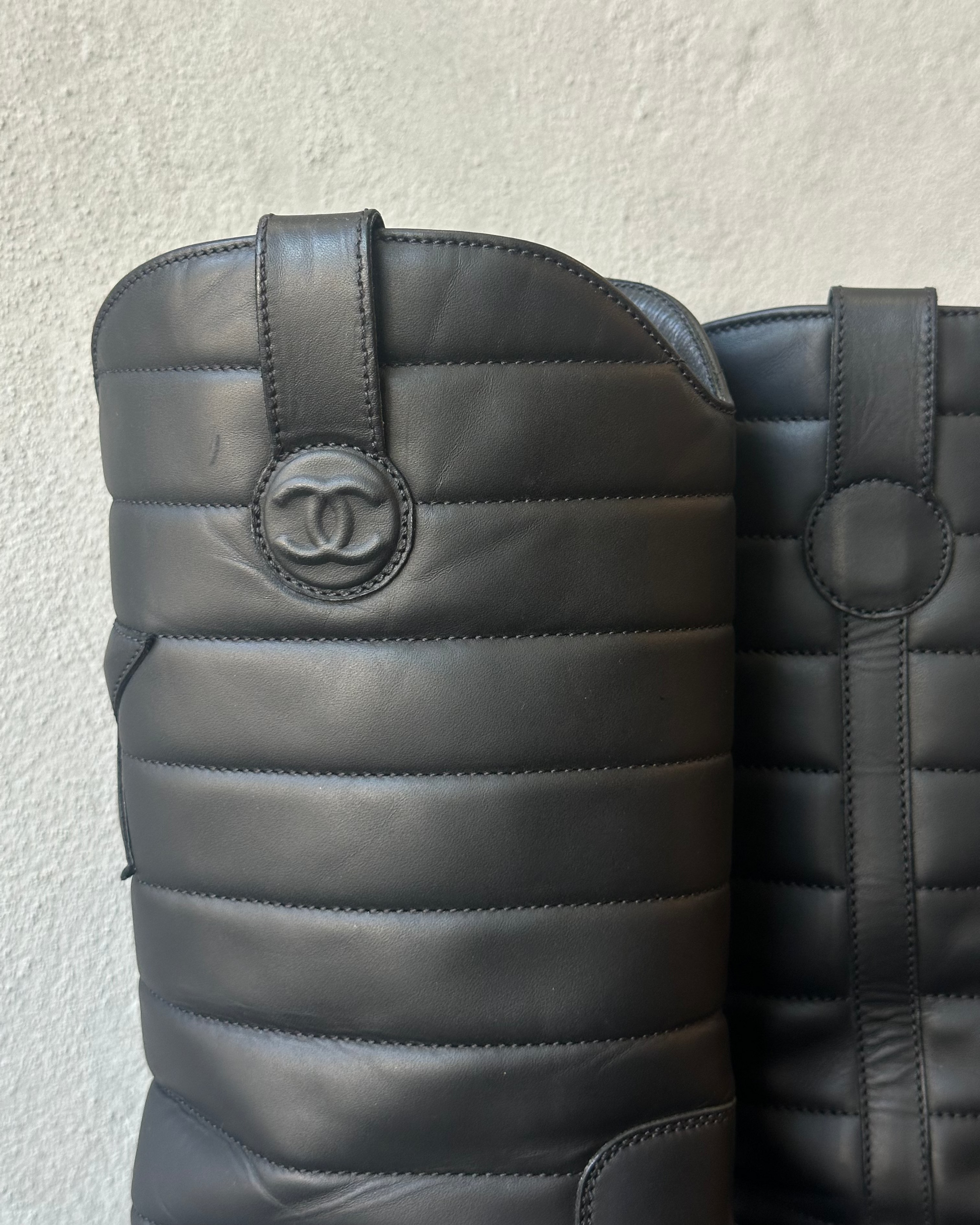 Black quilted leather boots with Chanel logo on a light gray background