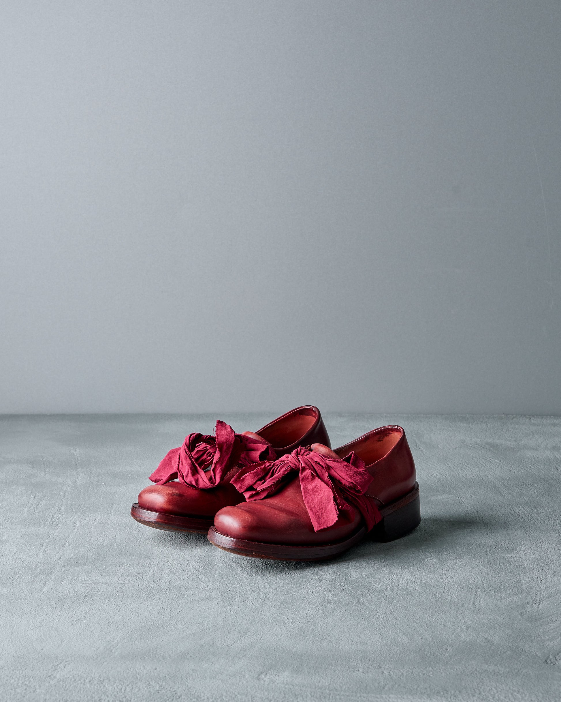 Red Cherevichkiotvichki  shoes with fabric bows on a gray surface and background