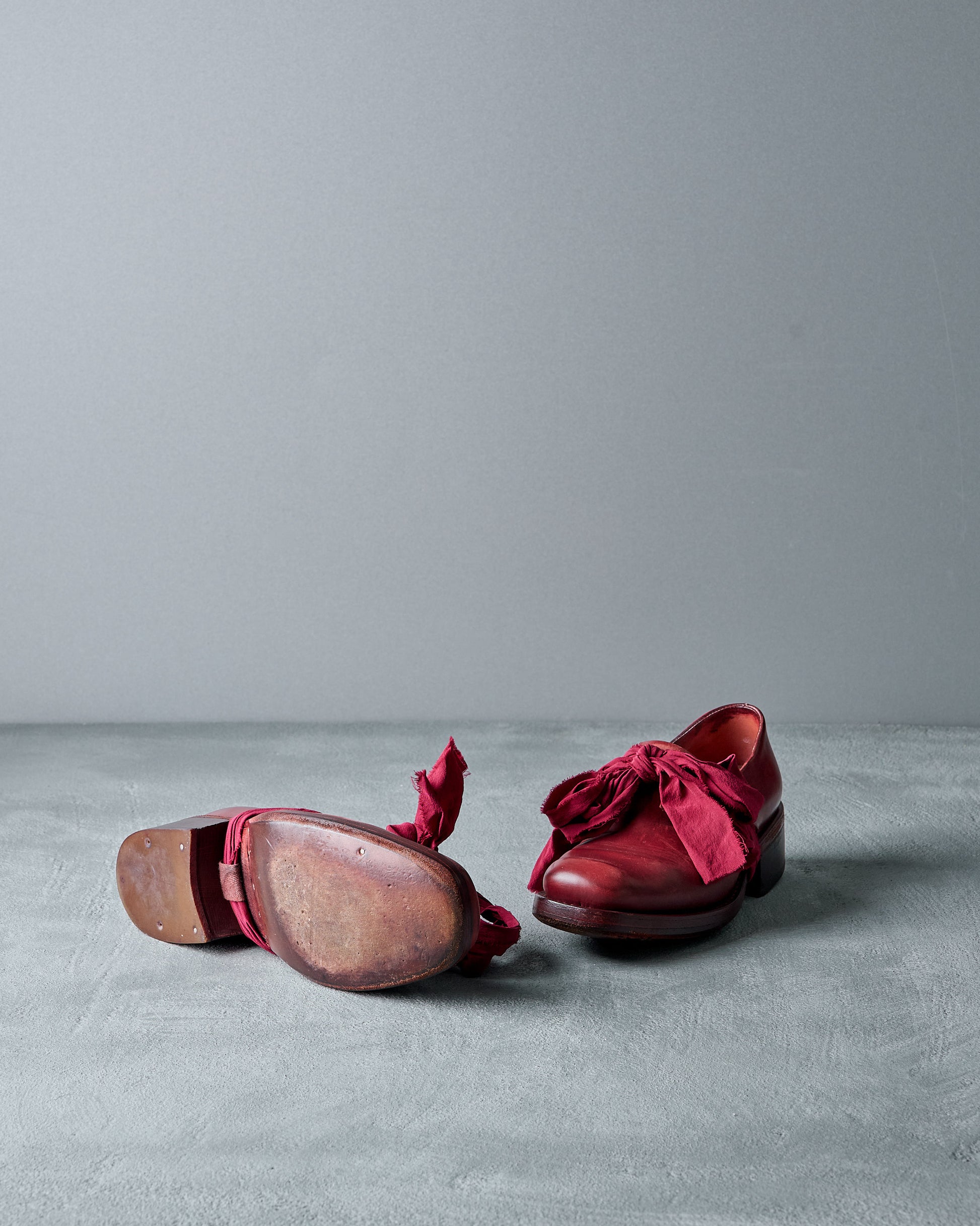 Pair of red Cherevichkiotvichki  shoes with wooden soles on a gray surface