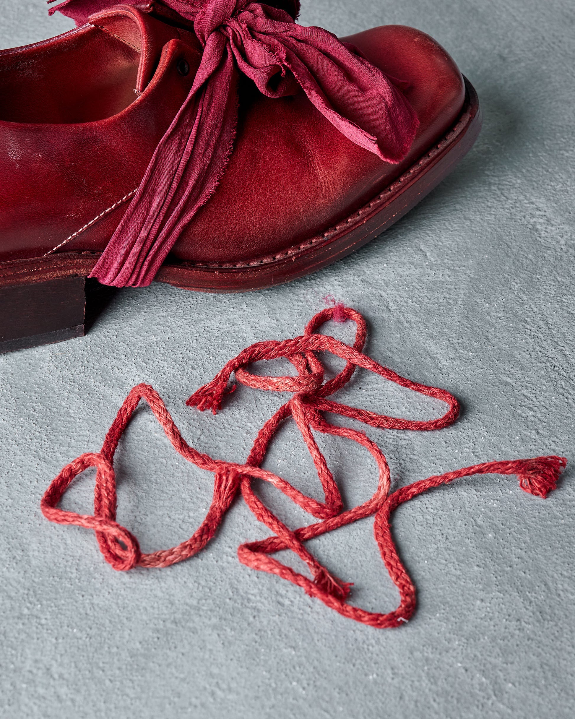 Red Cherevichkiotvichki  shoe with untied laces on a gray surface