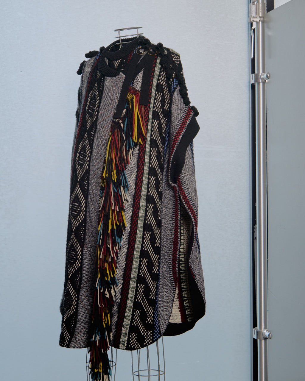 Colourful patterned Chloe poncho on a mannequin against a light blue wall.