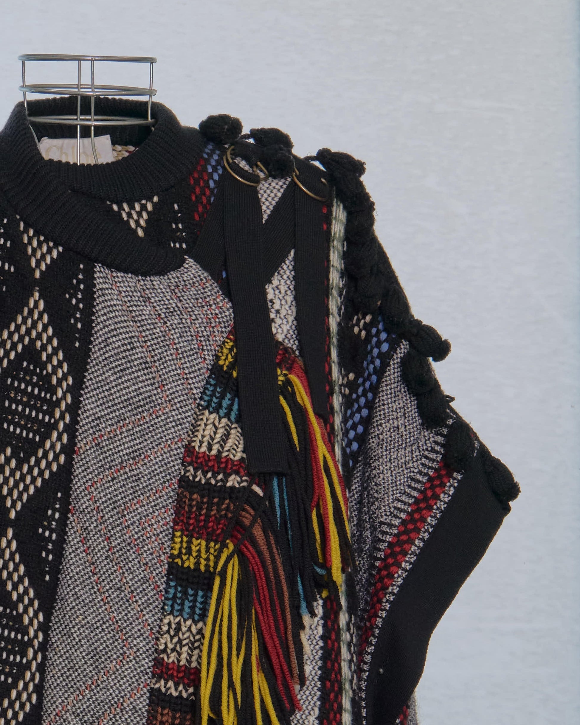 Colourful patterned Chloe poncho with tassels on a hanger against a light blue background