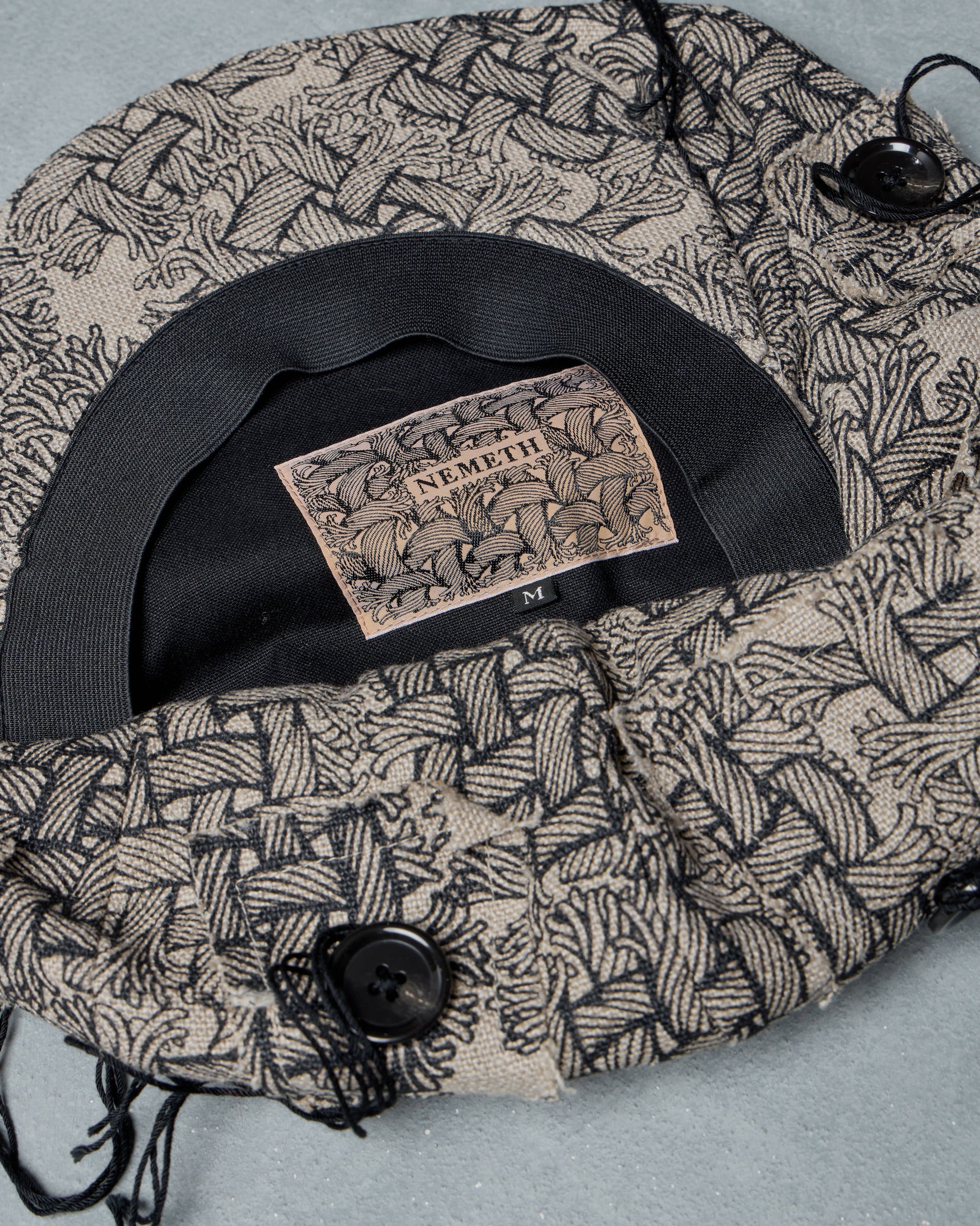 Patterned Christopher Nemeth  cap with a brand label on a light gray background