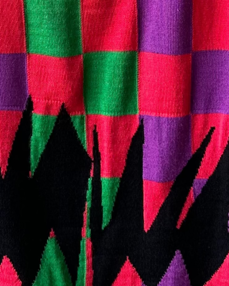 Colourful checkered Comme des Garcons vest on a hanger against a gray wall