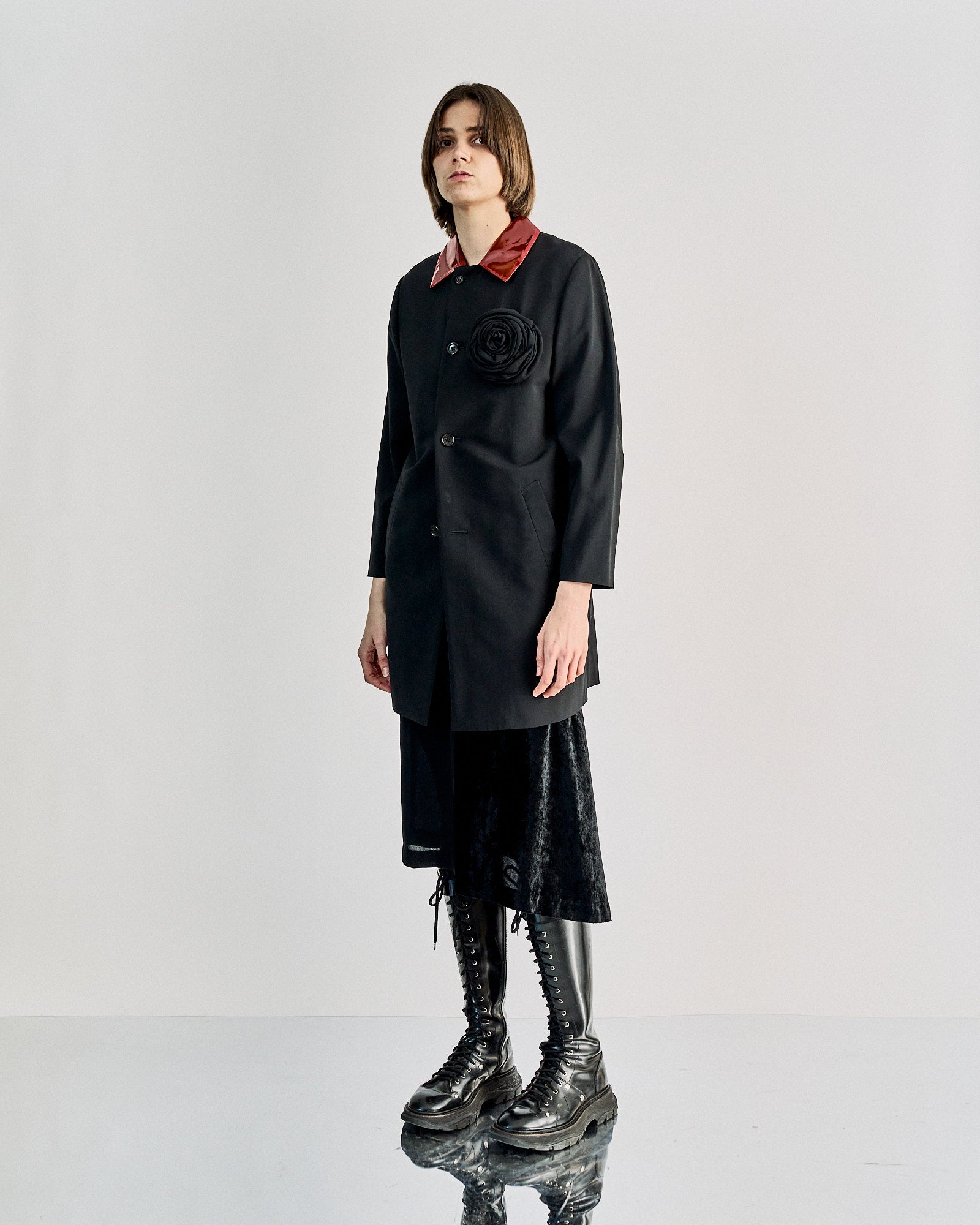 A person wears a chic black Comme des Garcons coat with a glossy red collar and a large black flower on the chest, conveying a sophisticated and stylish tone.