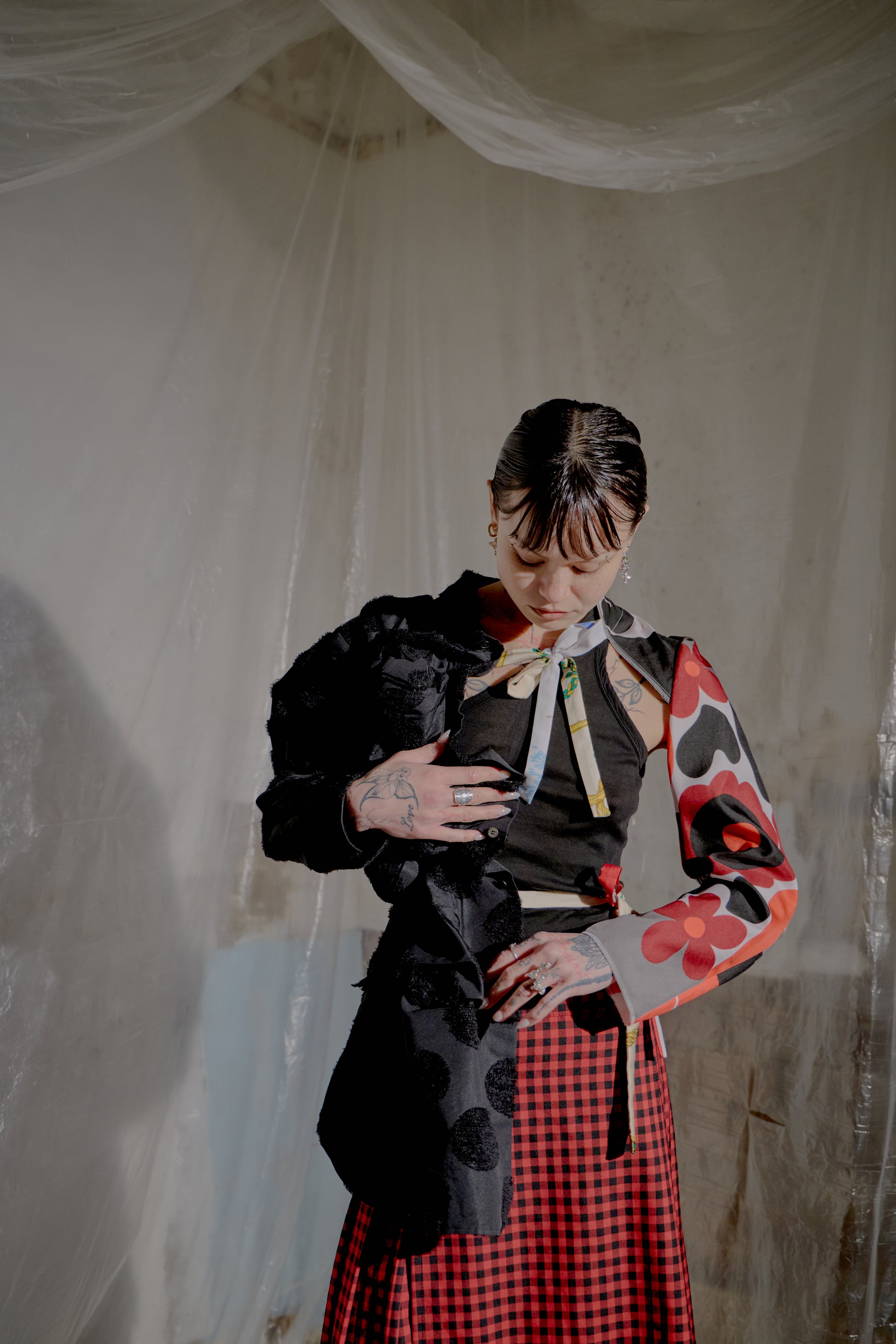 Person wearing a black and red Comme Des Garcons jacket and skirt in a room with white curtains